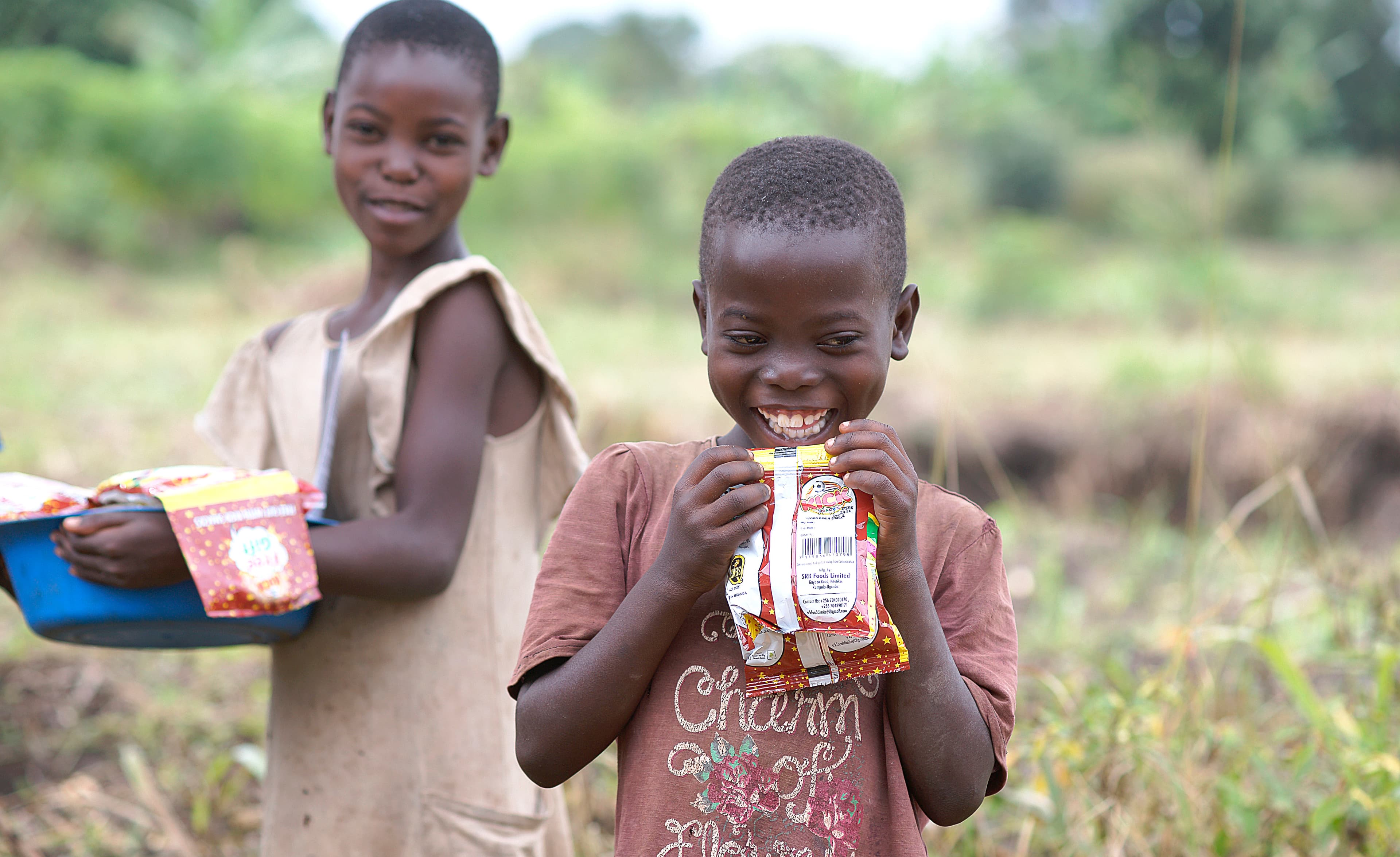 Two boys stand together eating snack packages.