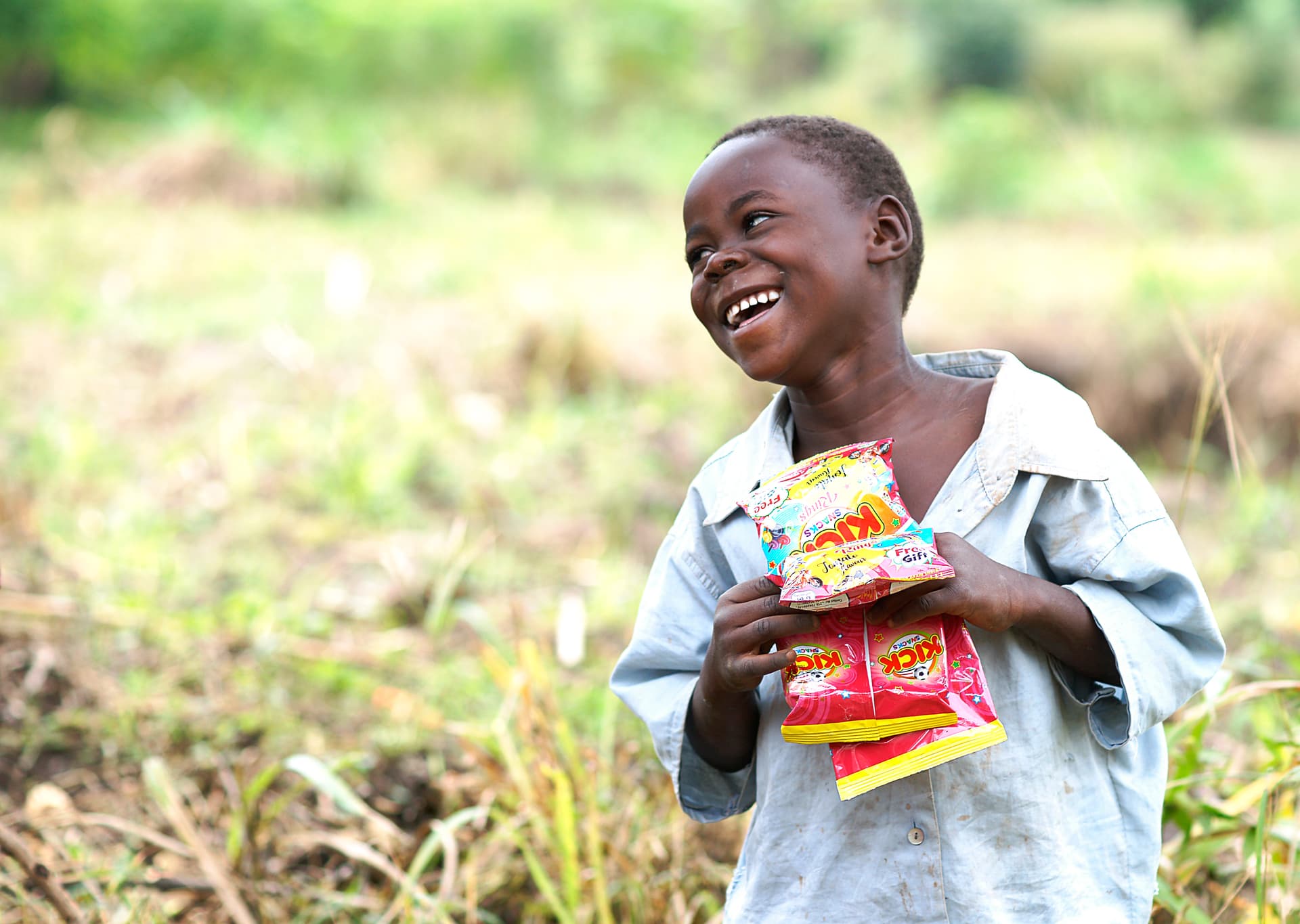 Smiling boy holds food packages against his chest in a field.