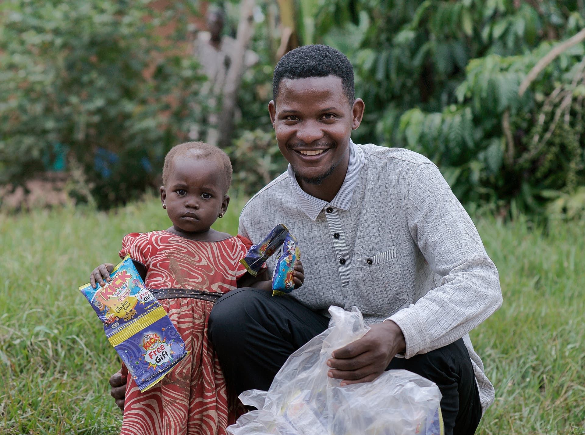 Man kneels to hand a food package to a young girl as another boy watches.