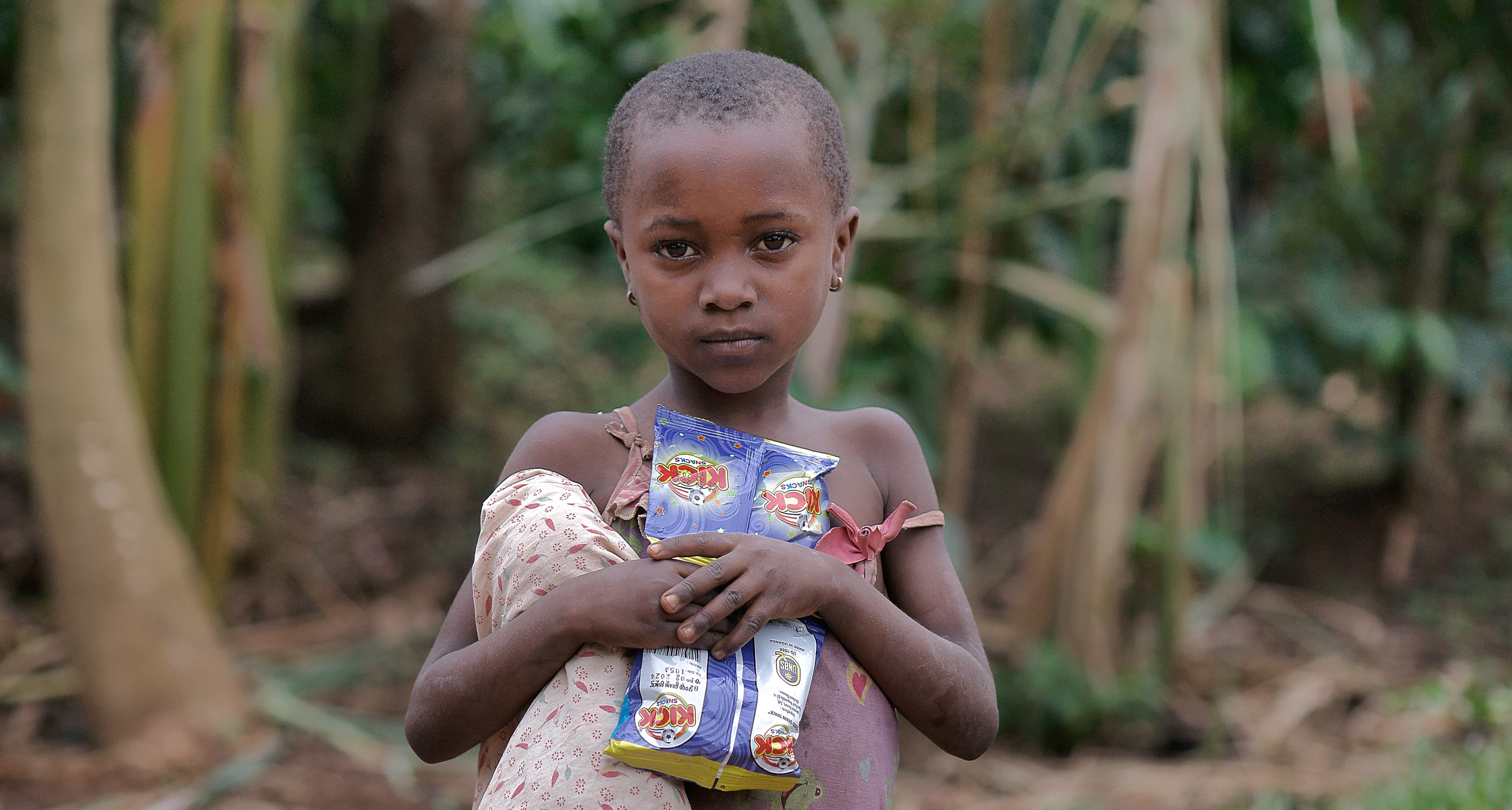 Young girl holds a food package while standing in tall grass.