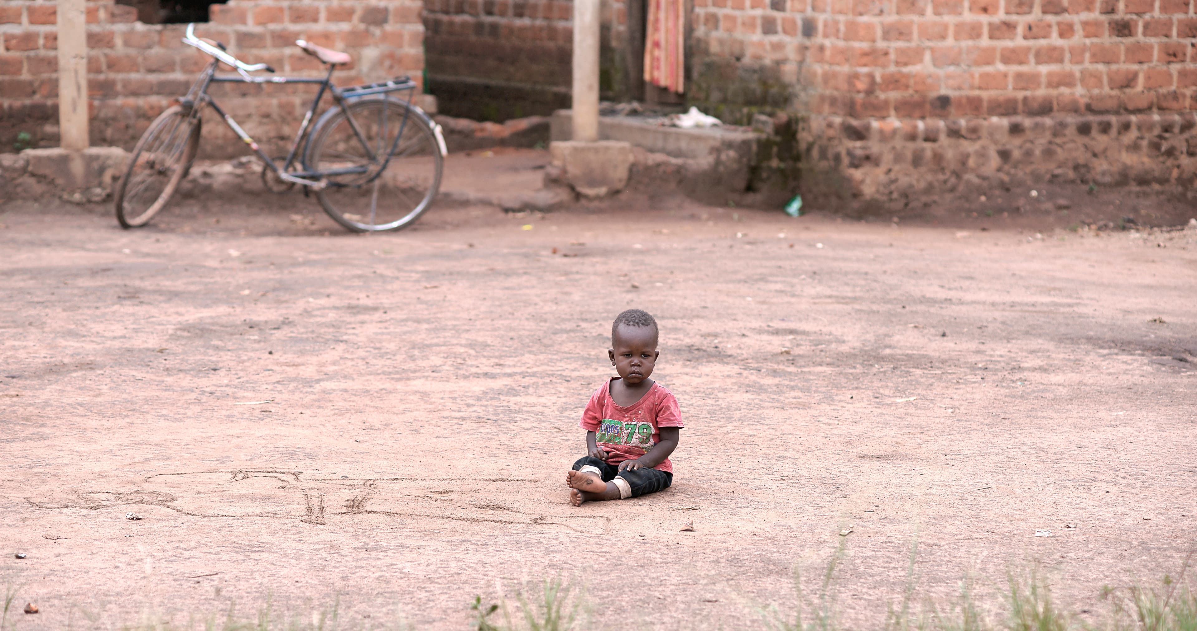 Toddler sits alone on the ground outdoors.