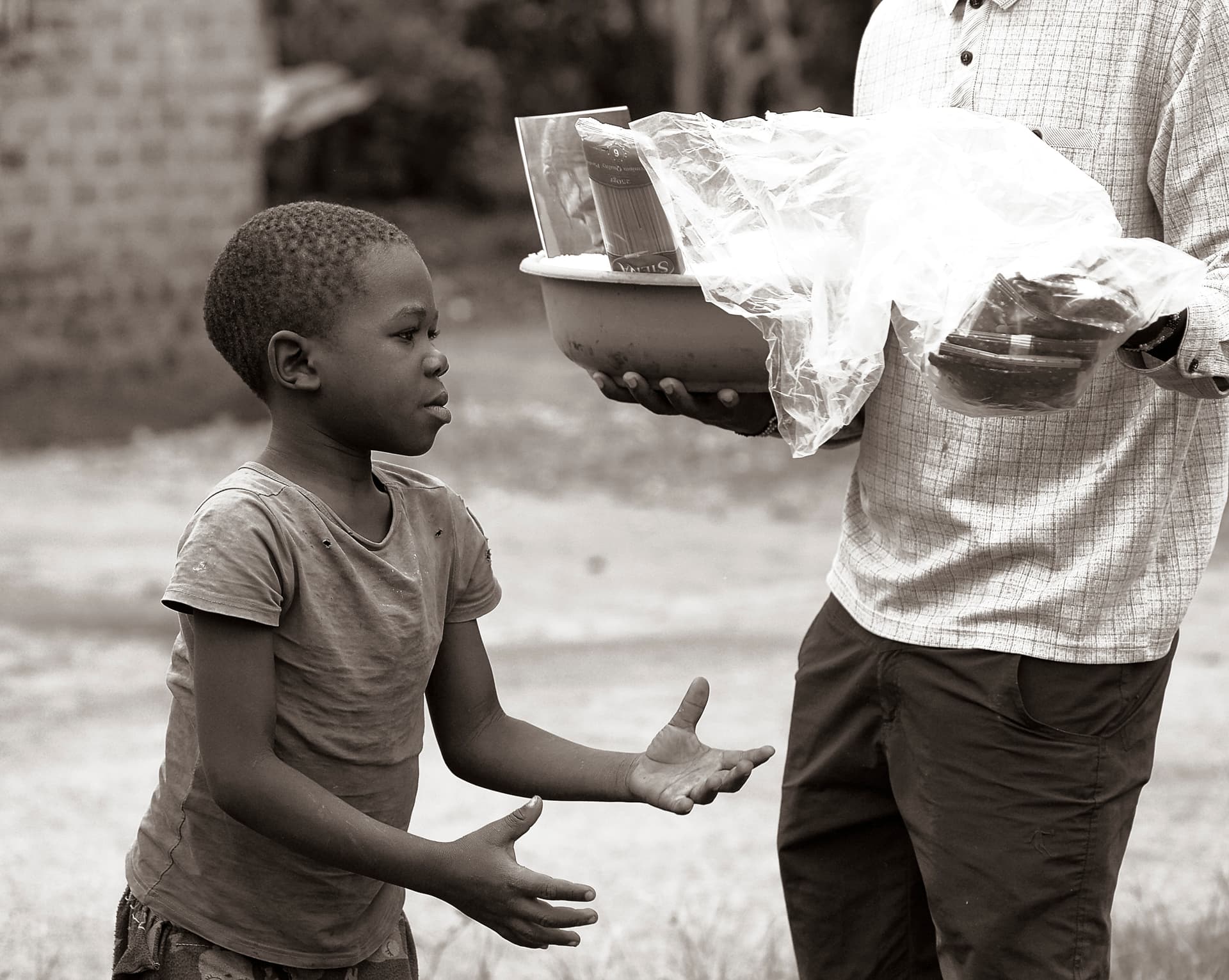 Man in a patterned shirt hands a food item to a young boy outdoors.