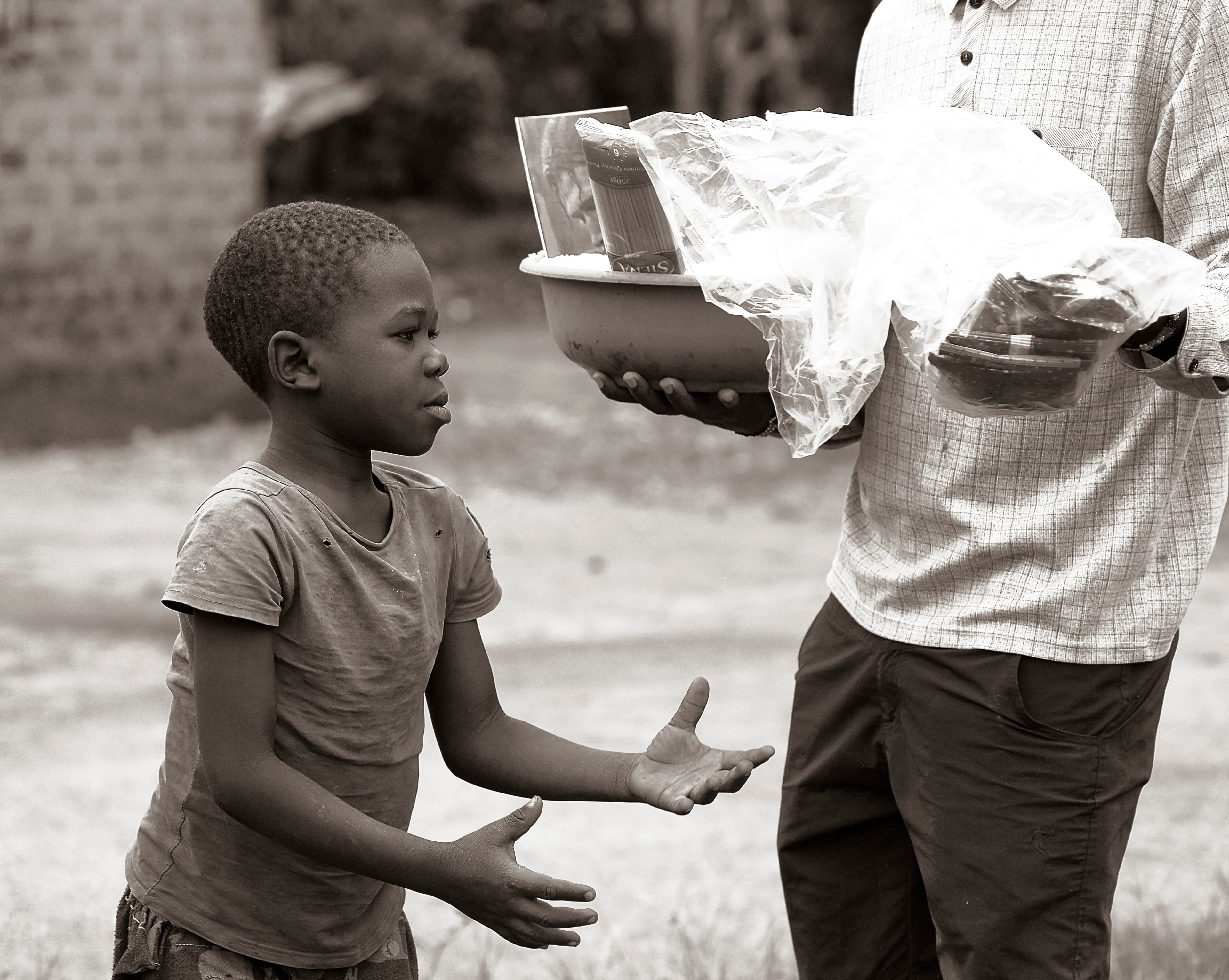 Man in a patterned shirt hands a food item to a young boy outdoors.