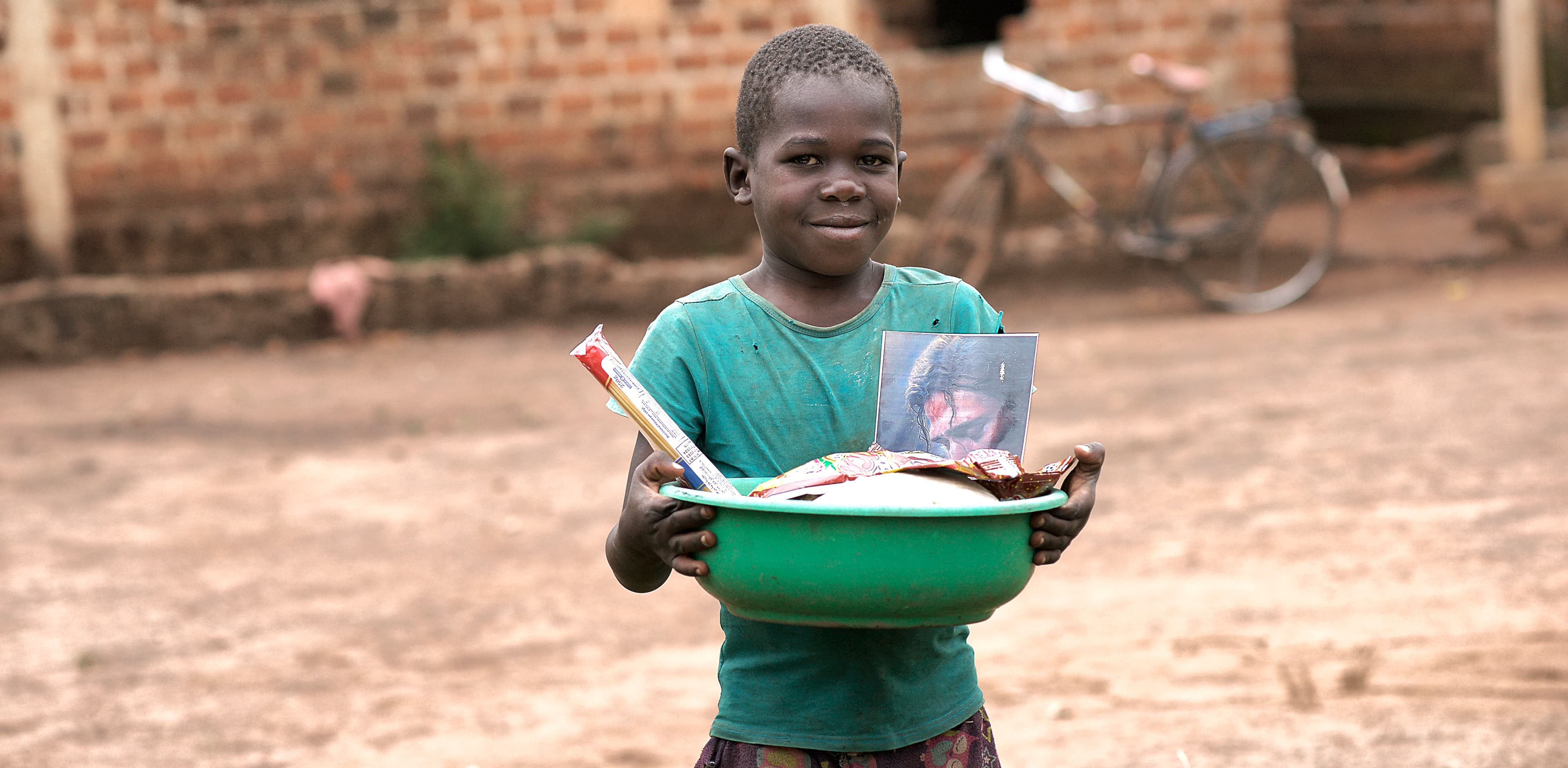 Boy holds a white basin filled with food items while standing outdoors.