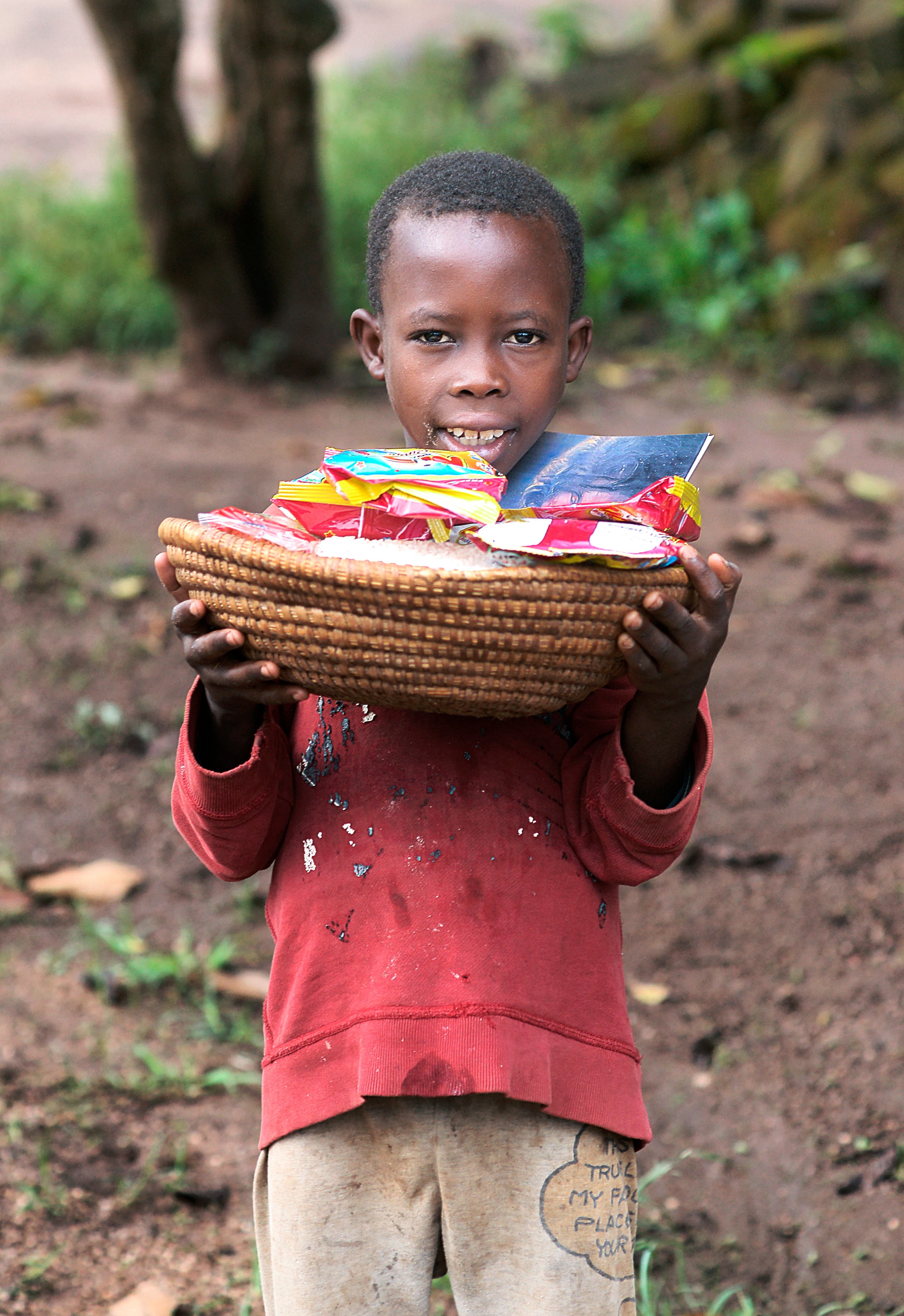 Boy carries a woven basket of food items on his head.