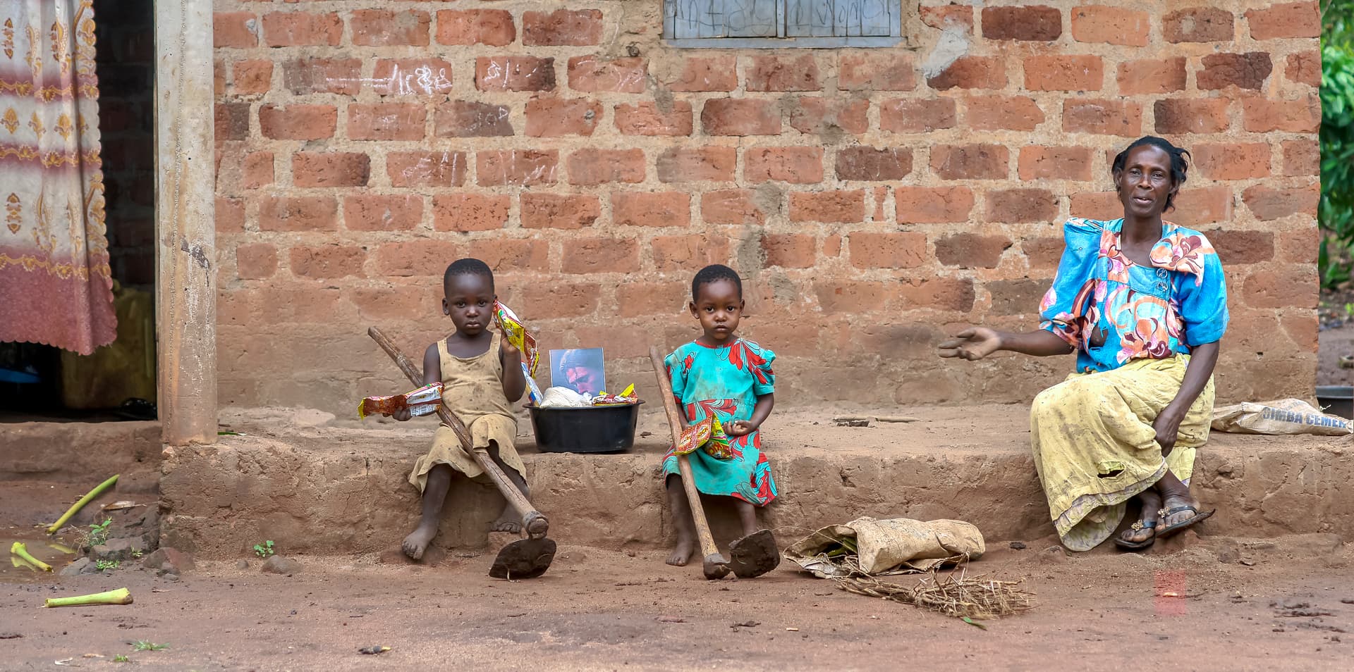 Woman sits with two young children outside a brick home.