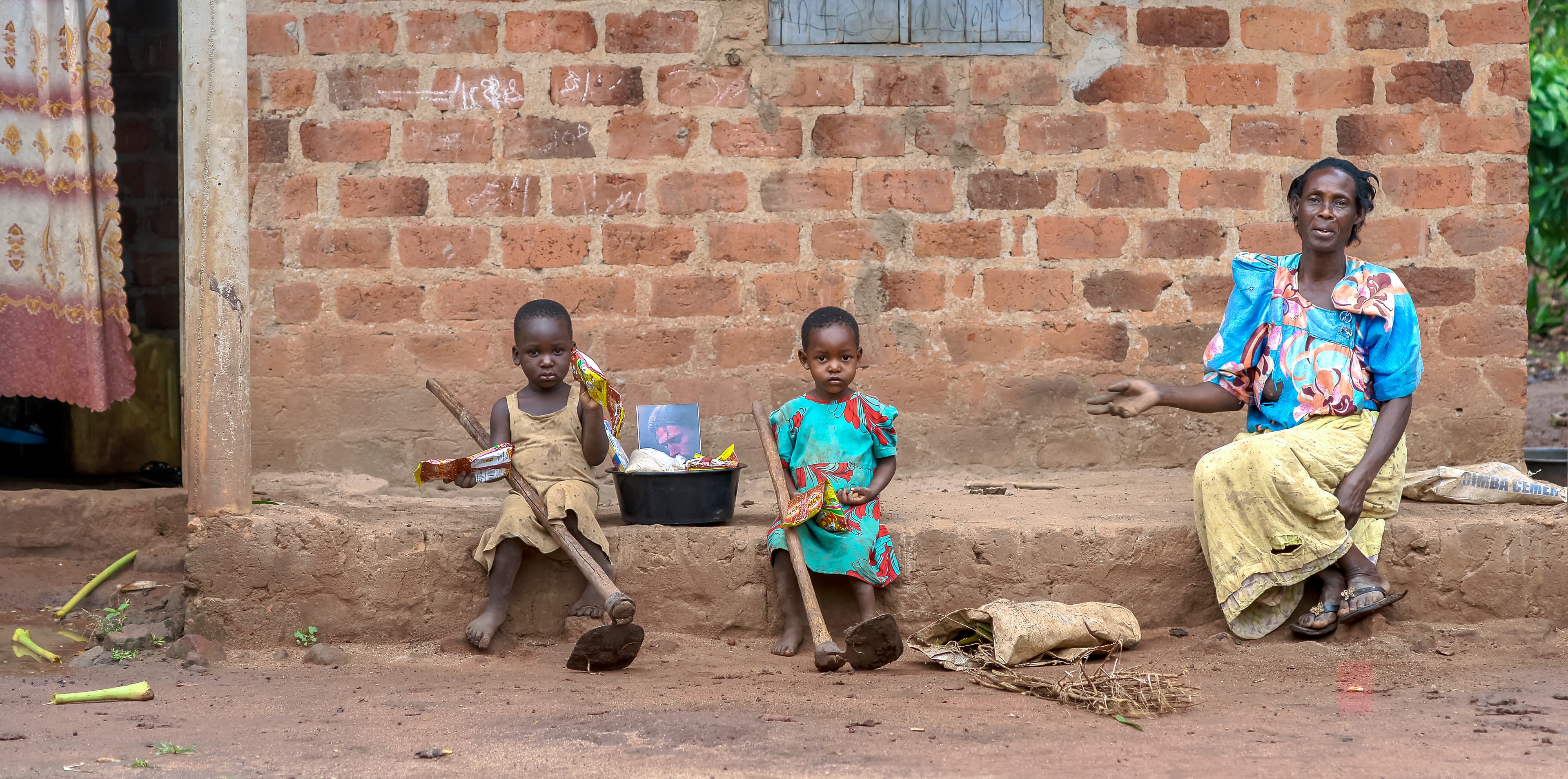 Woman sits with two young children outside a brick home.