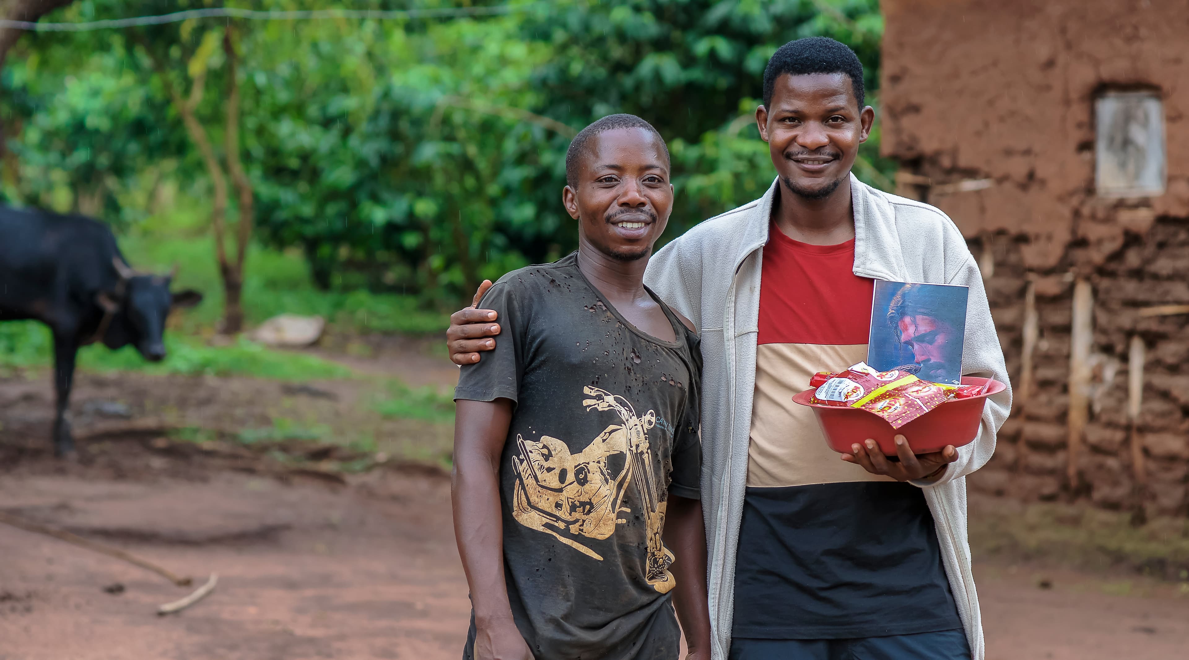 Two smiling men stand together, one holding a red food package.