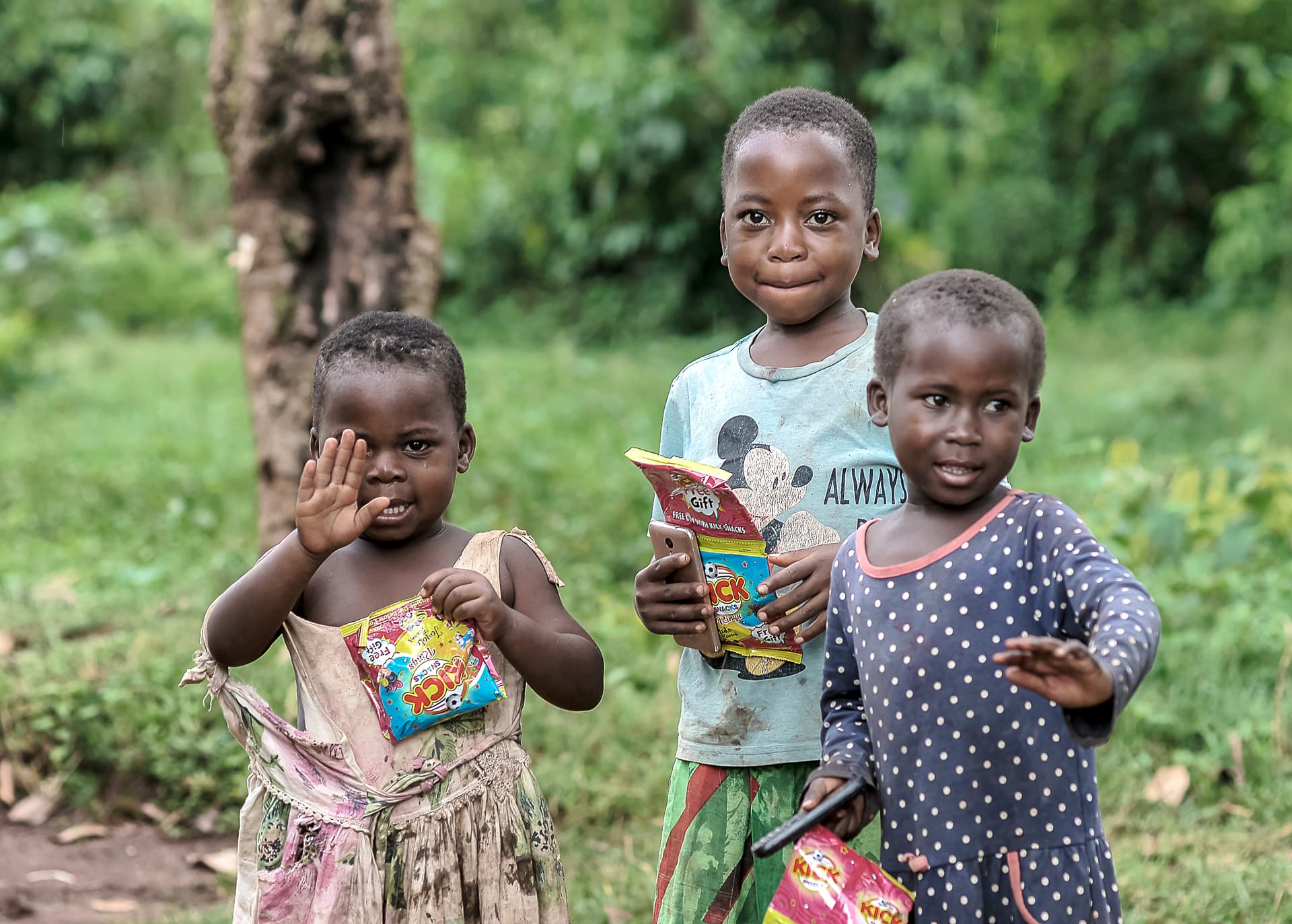 Two children wave while holding food packages outdoors.