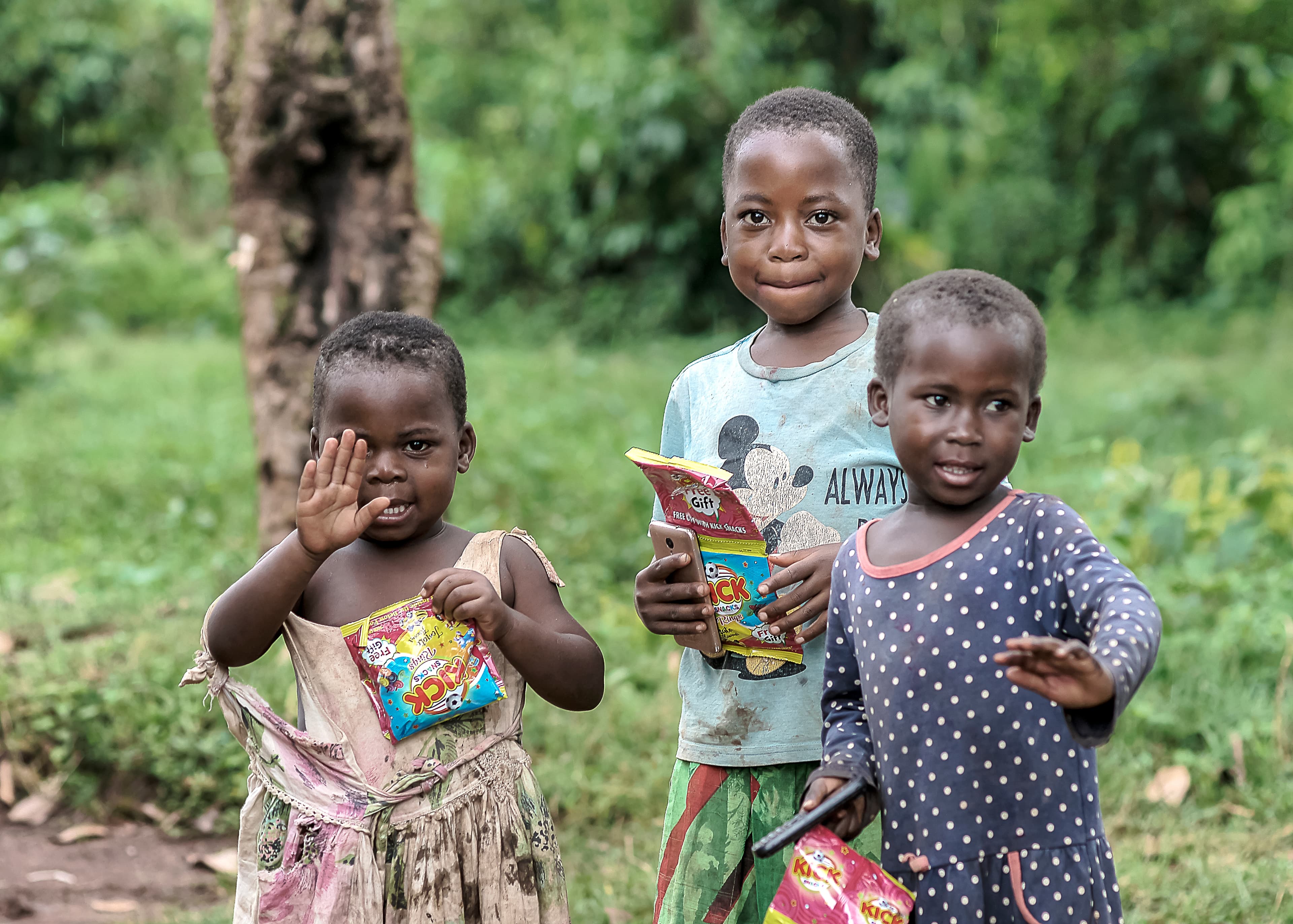 Two children wave while holding food packages outdoors.