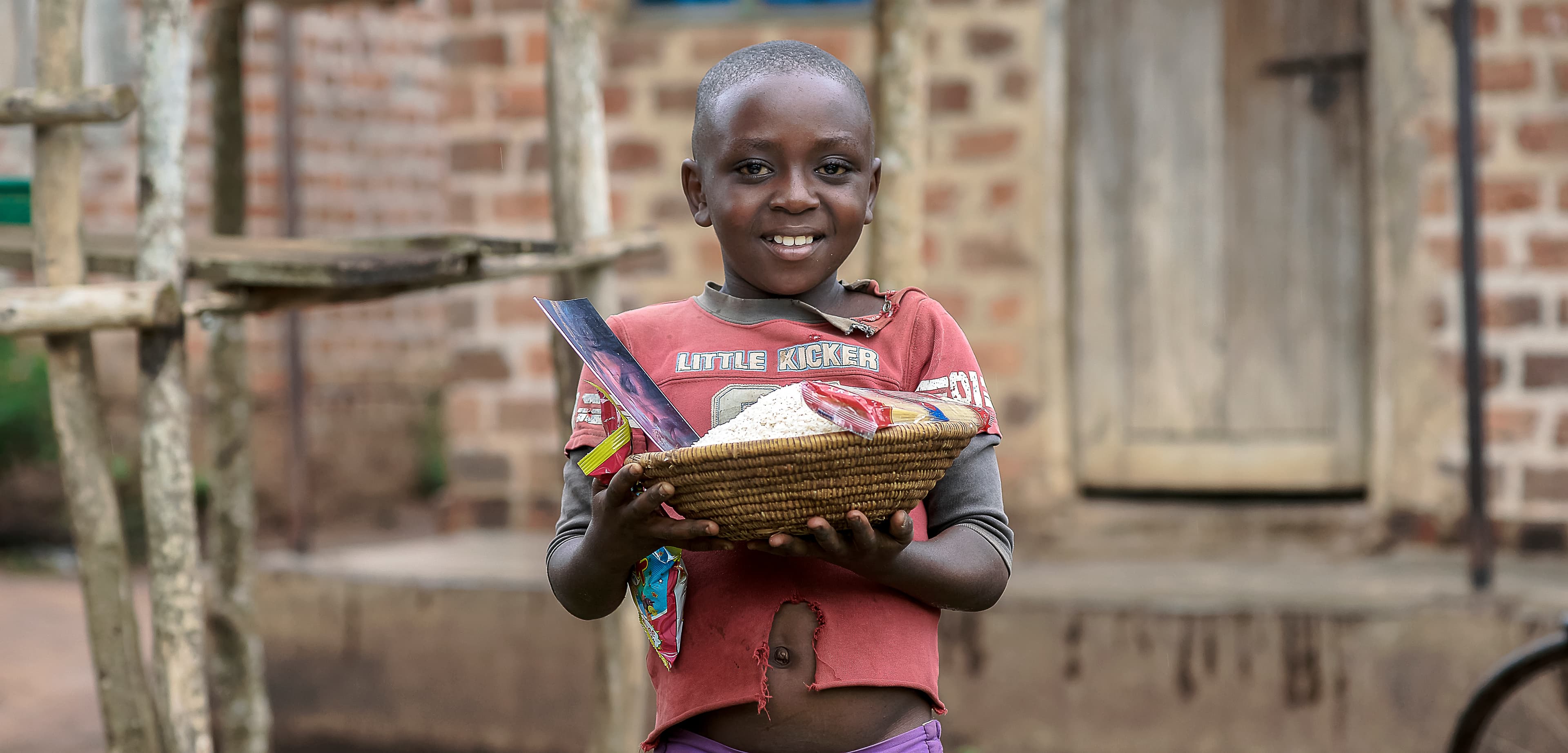 Boy holds a food-filled basket while standing near a brick wall.