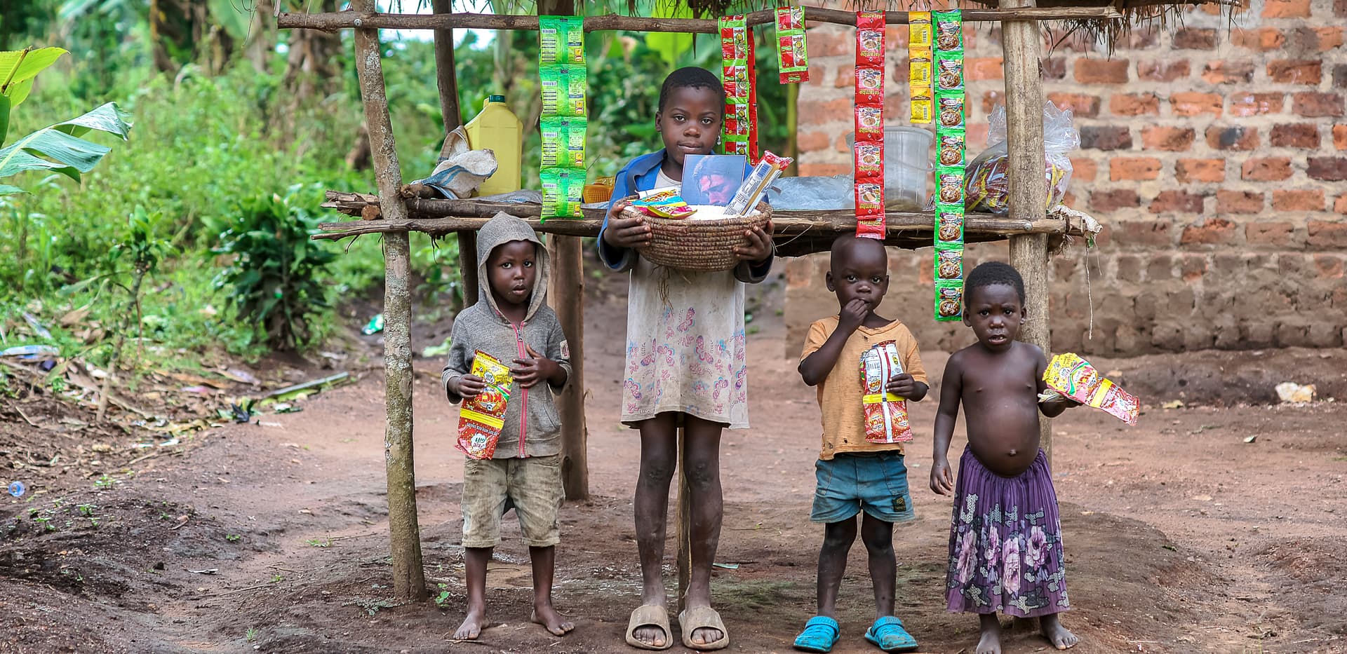 Children stand near a wooden pole fence outside a brick building.