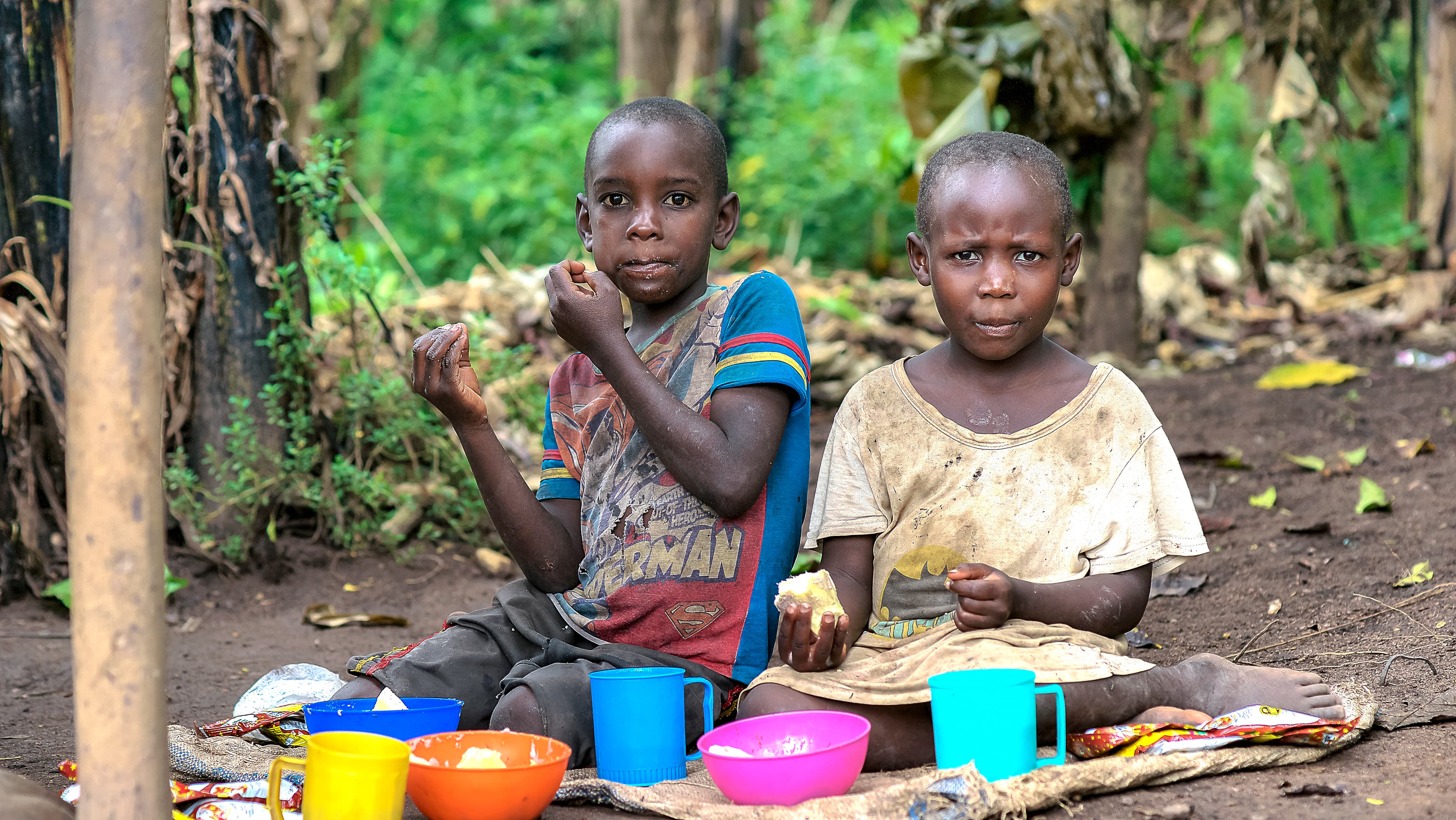 Two children sit on the ground surrounded by colorful cups and bowls.