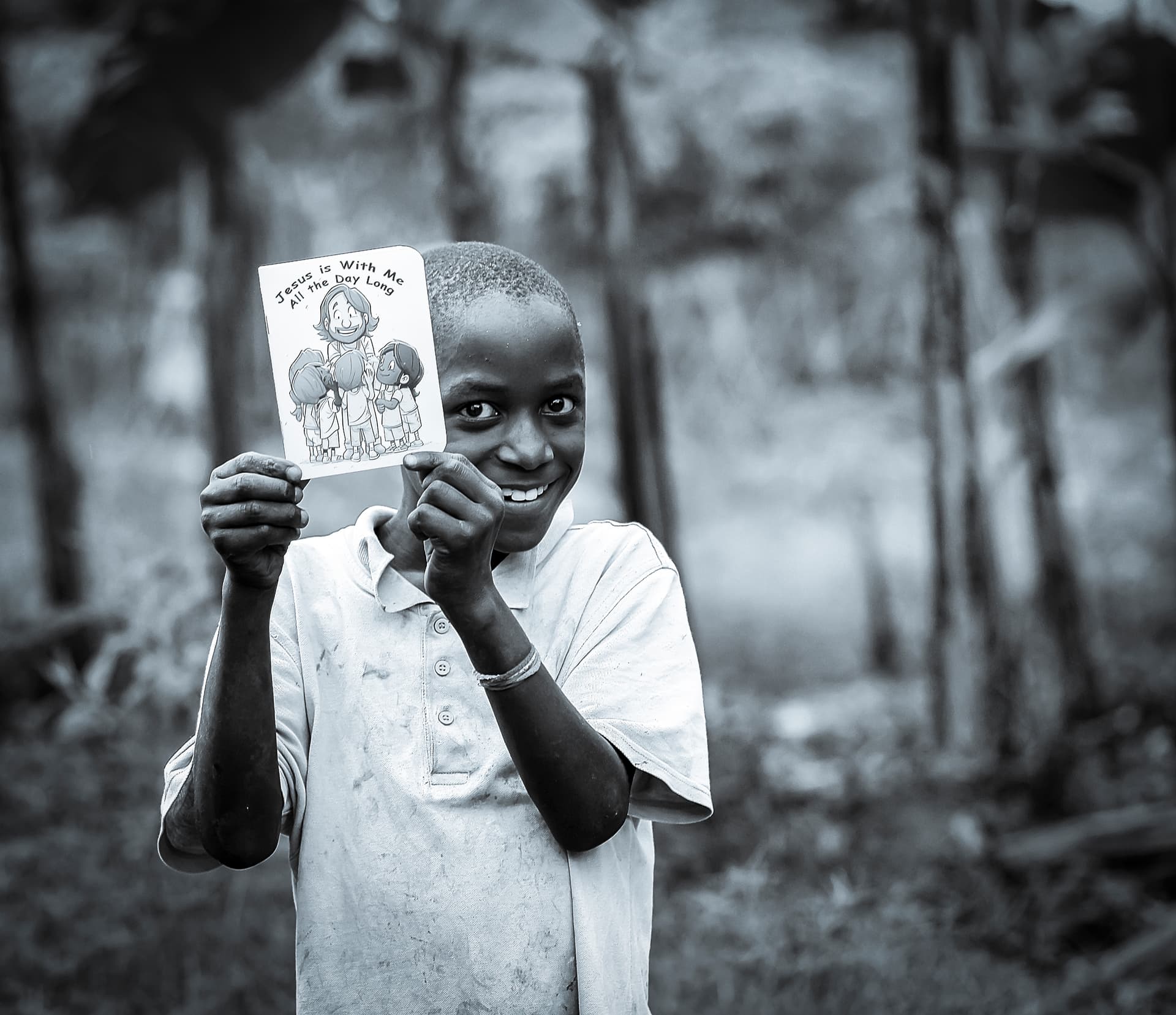 Black and white photo of a boy holding up a gospel tract booklet toward the camera.