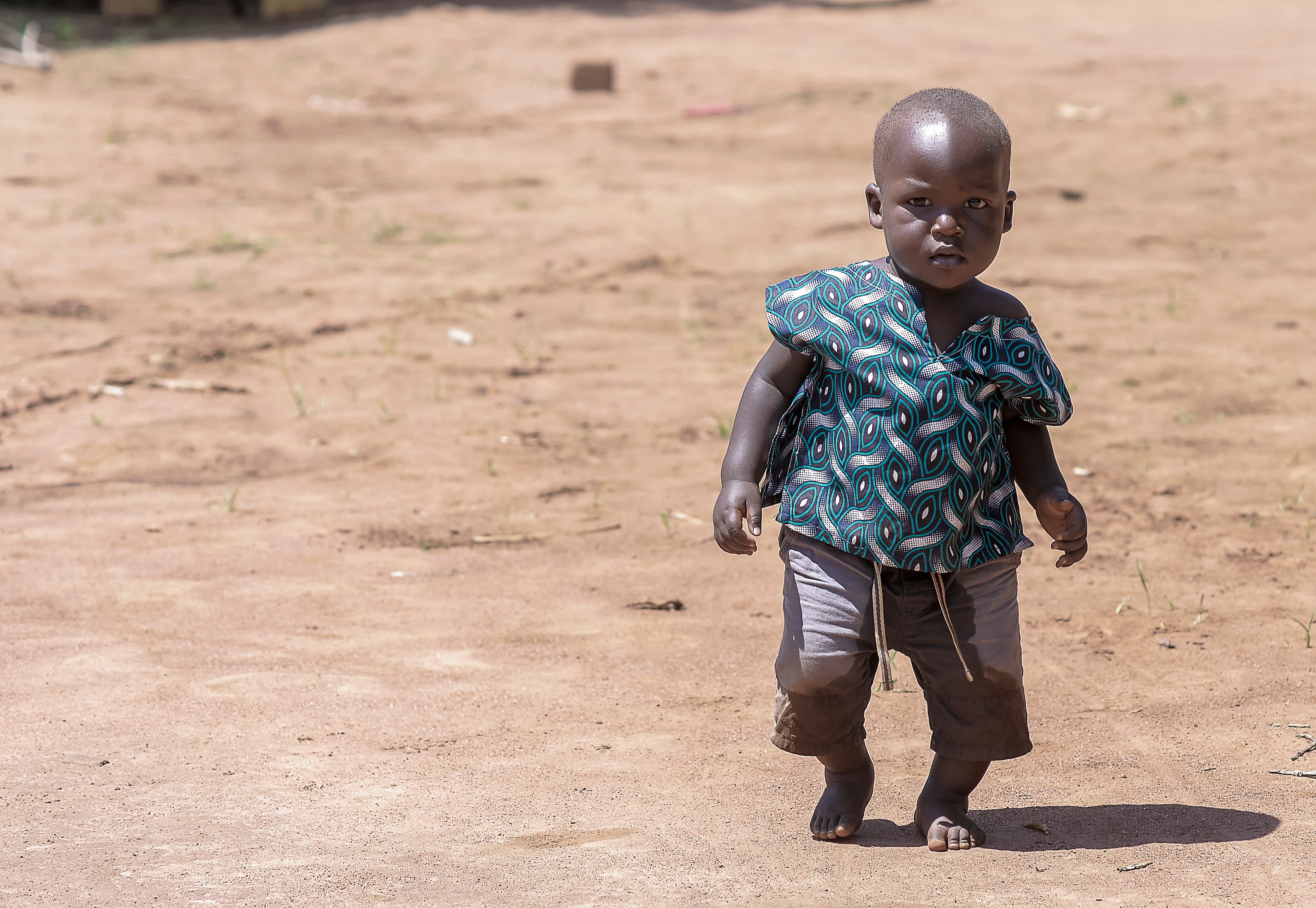 A young child stands alone on a dirt path in the village.