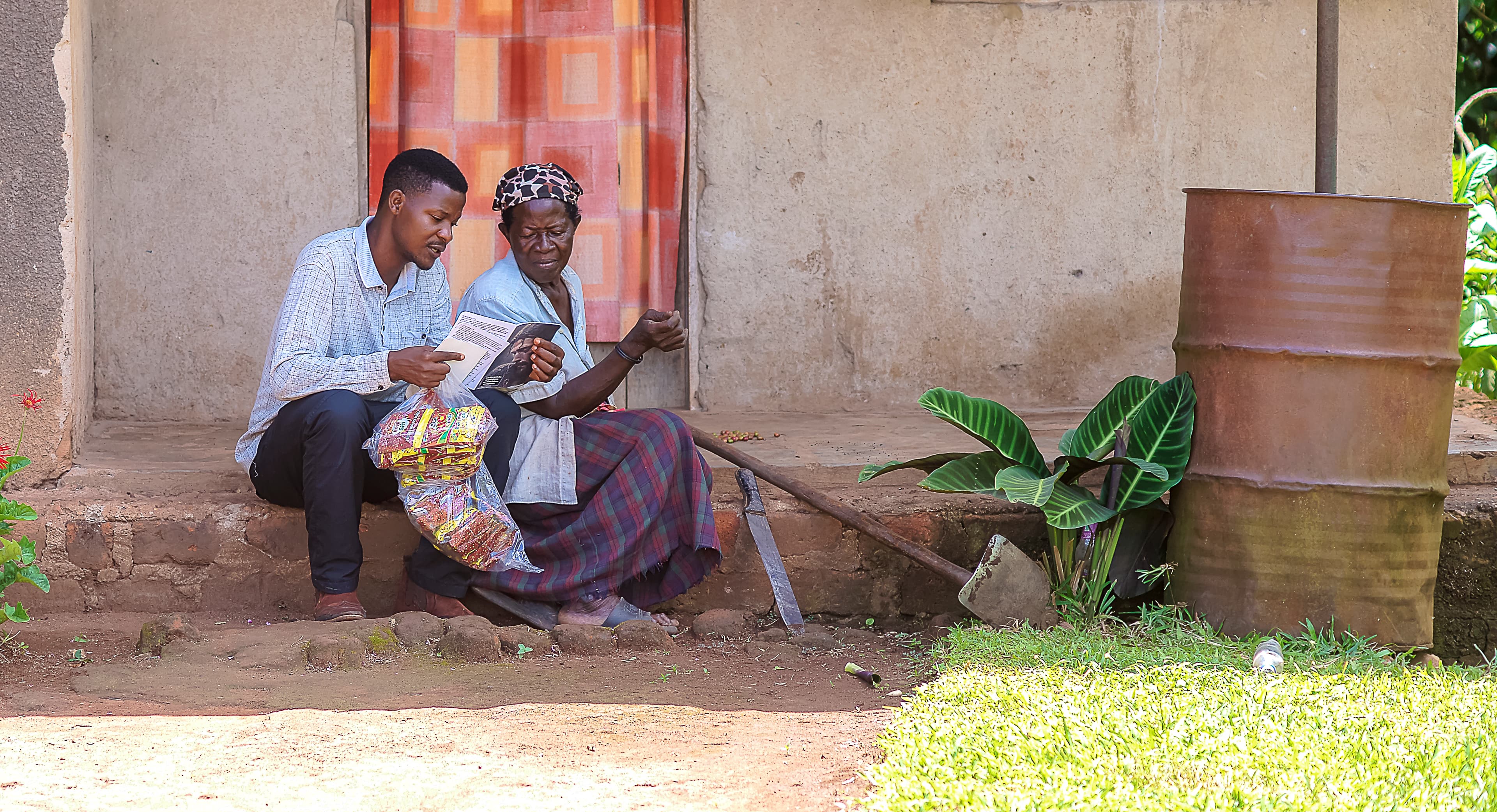An elderly man and woman sit together on a porch outside a house.