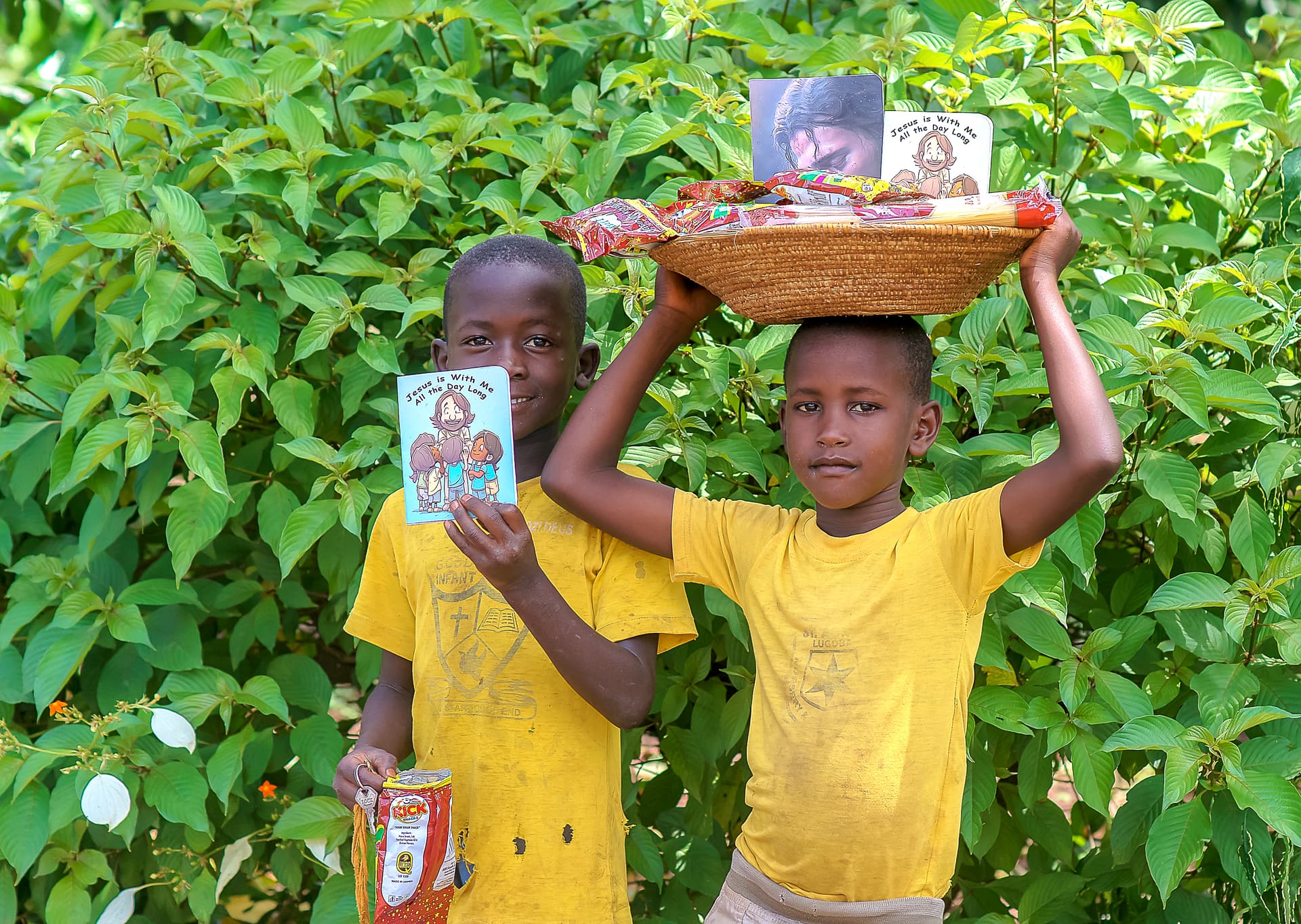 Two boys in matching yellow shirts balance a tray of food and a booklet together on their heads.