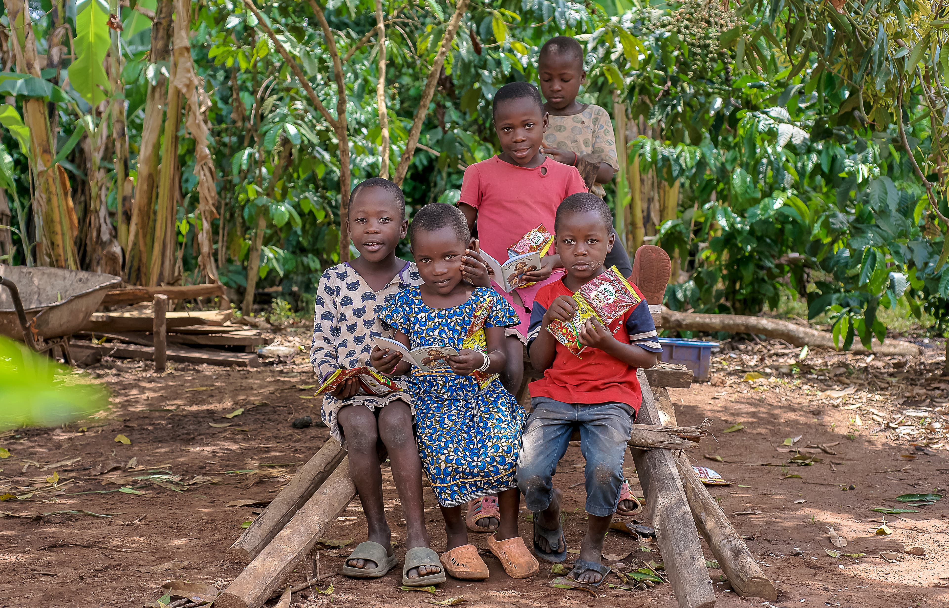A group of children and an adult sit together on a wooden bench outdoors.