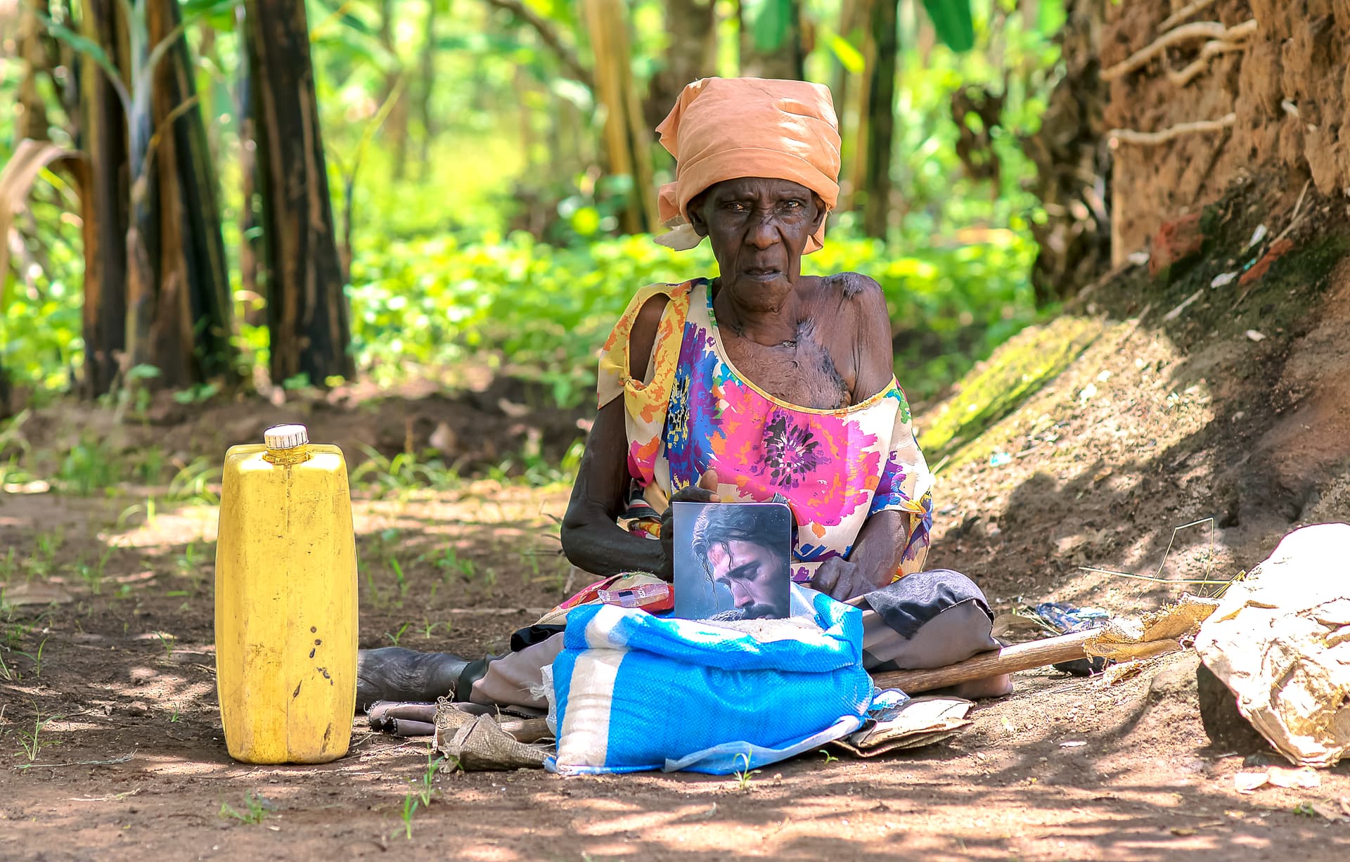 A JFM volunteer converses with Elder Atim Justine as she sits beside a food package and jerry can.