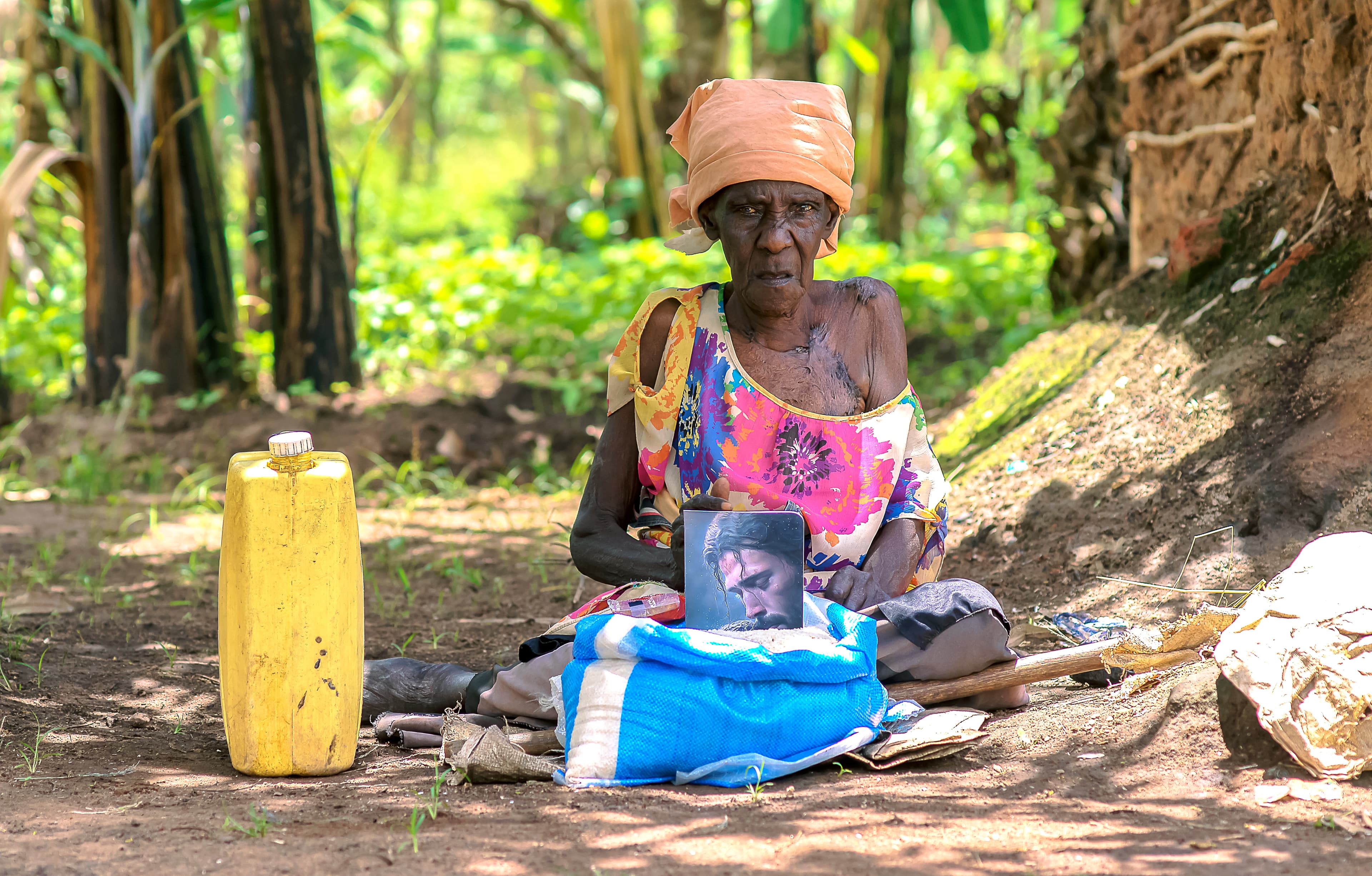 A JFM volunteer converses with Elder Atim Justine as she sits beside a food package and jerry can.