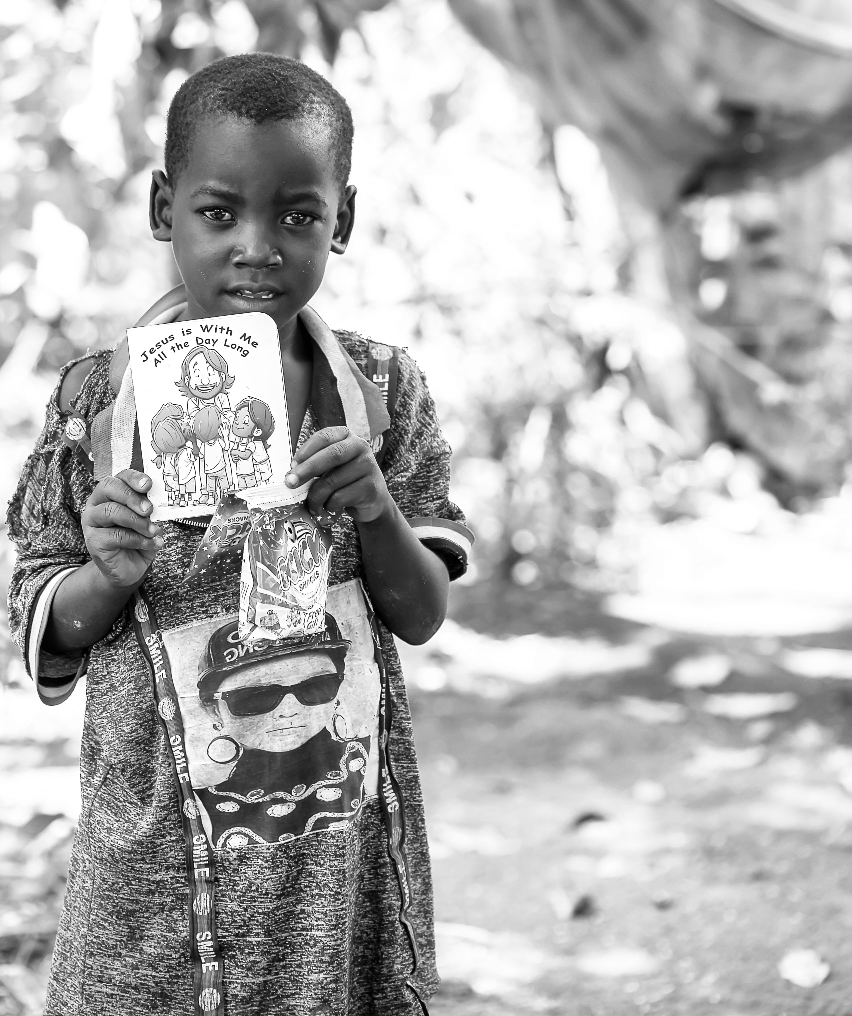 Black and white close-up of a boy holding a children's Bible booklet with an illustrated cover.