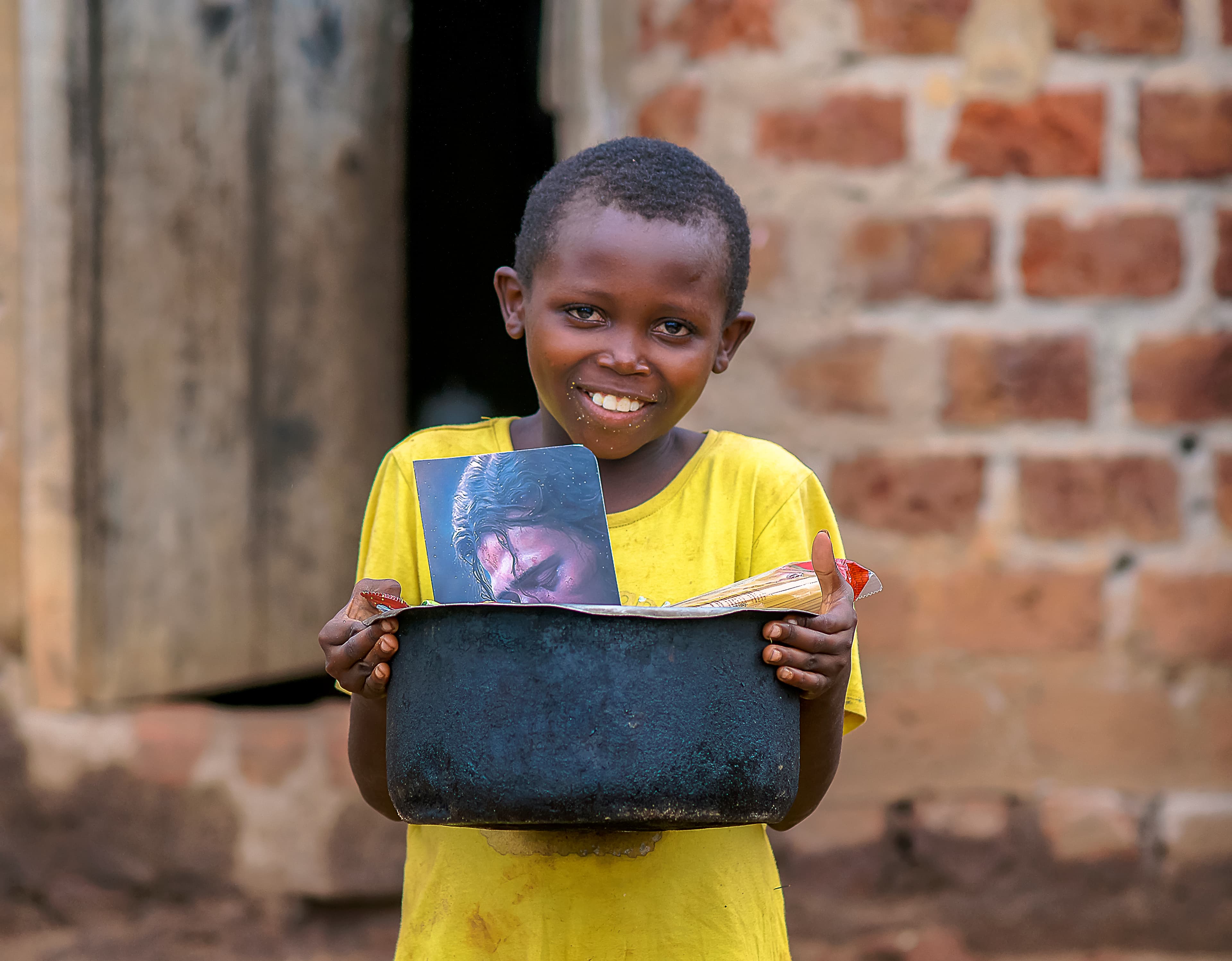 A boy stands in a brick building doorway holding a photo card and food package.