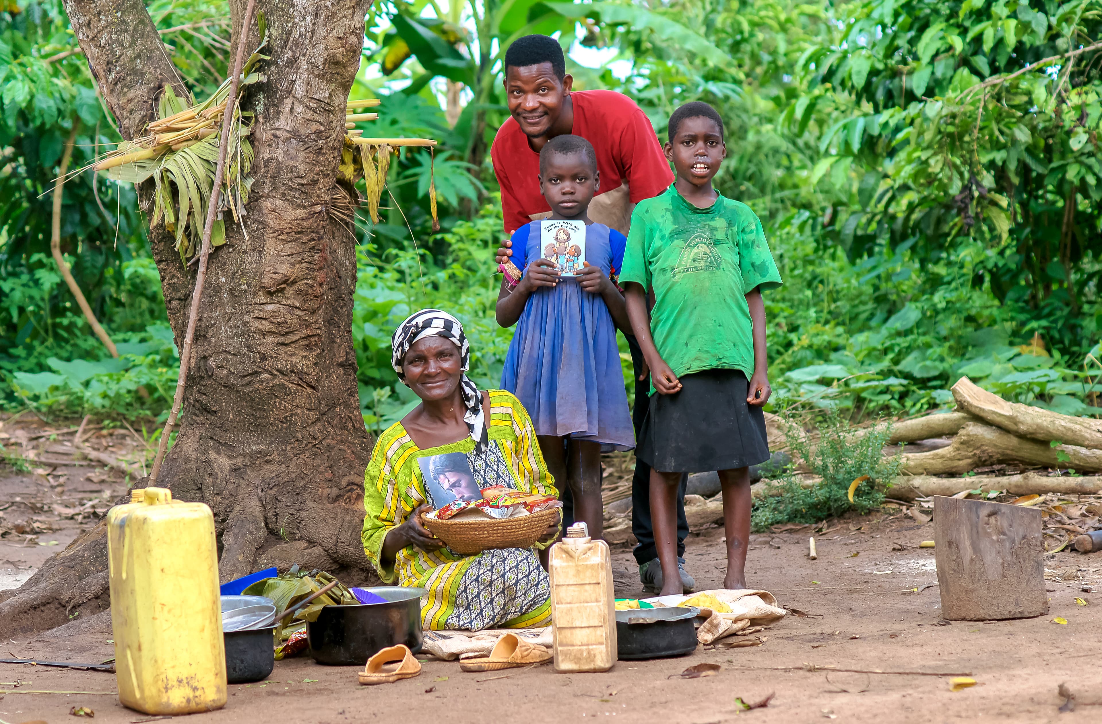 A woman and several children sit outdoors surrounded by jerry cans and household supplies.