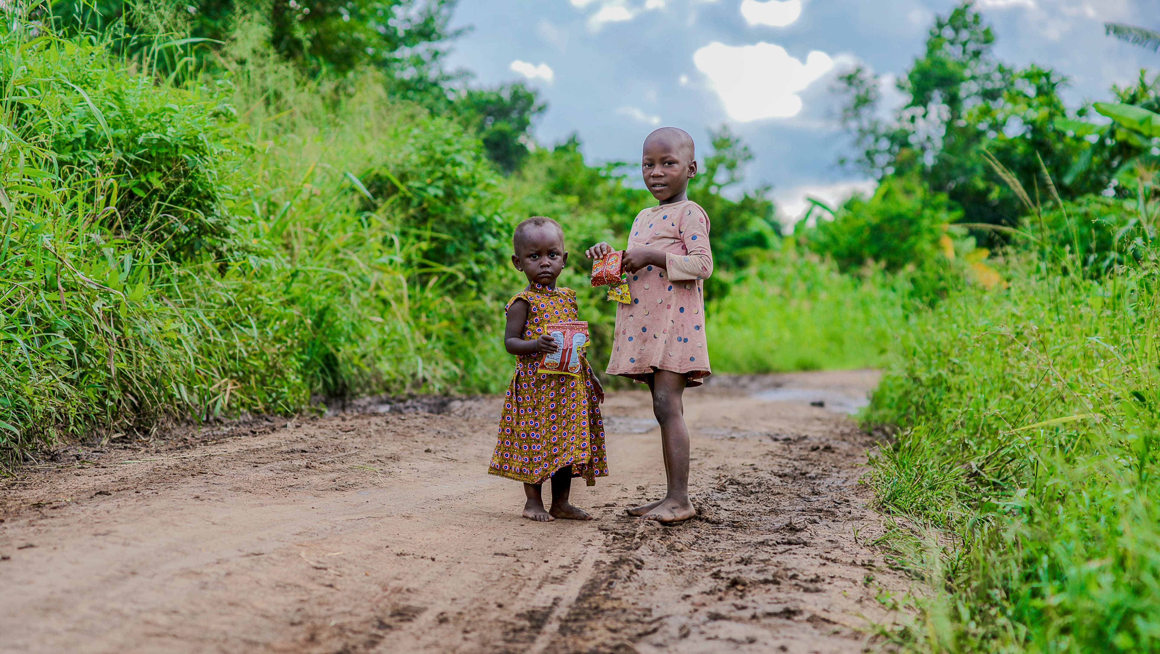 Two children walk together along a dirt path in the distance.