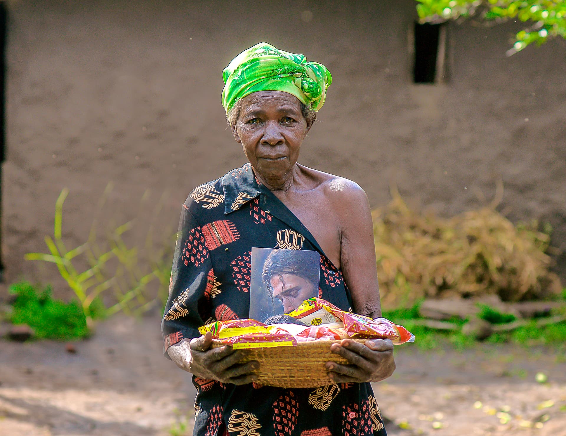 Elder Sylvia stands outdoors holding a food gift package, matching an earlier photo.