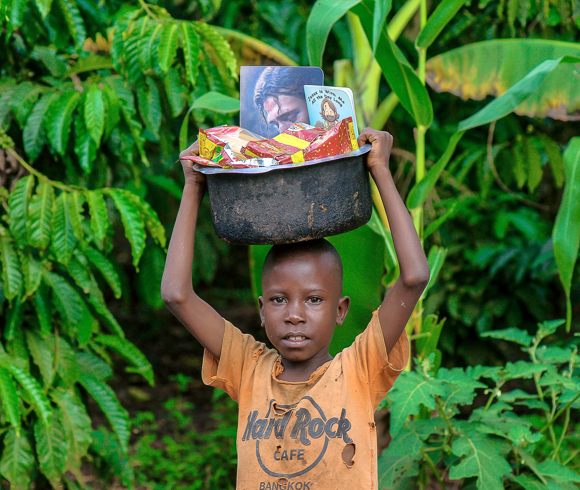 A boy carries a black basin loaded with food gift packages balanced on his head.