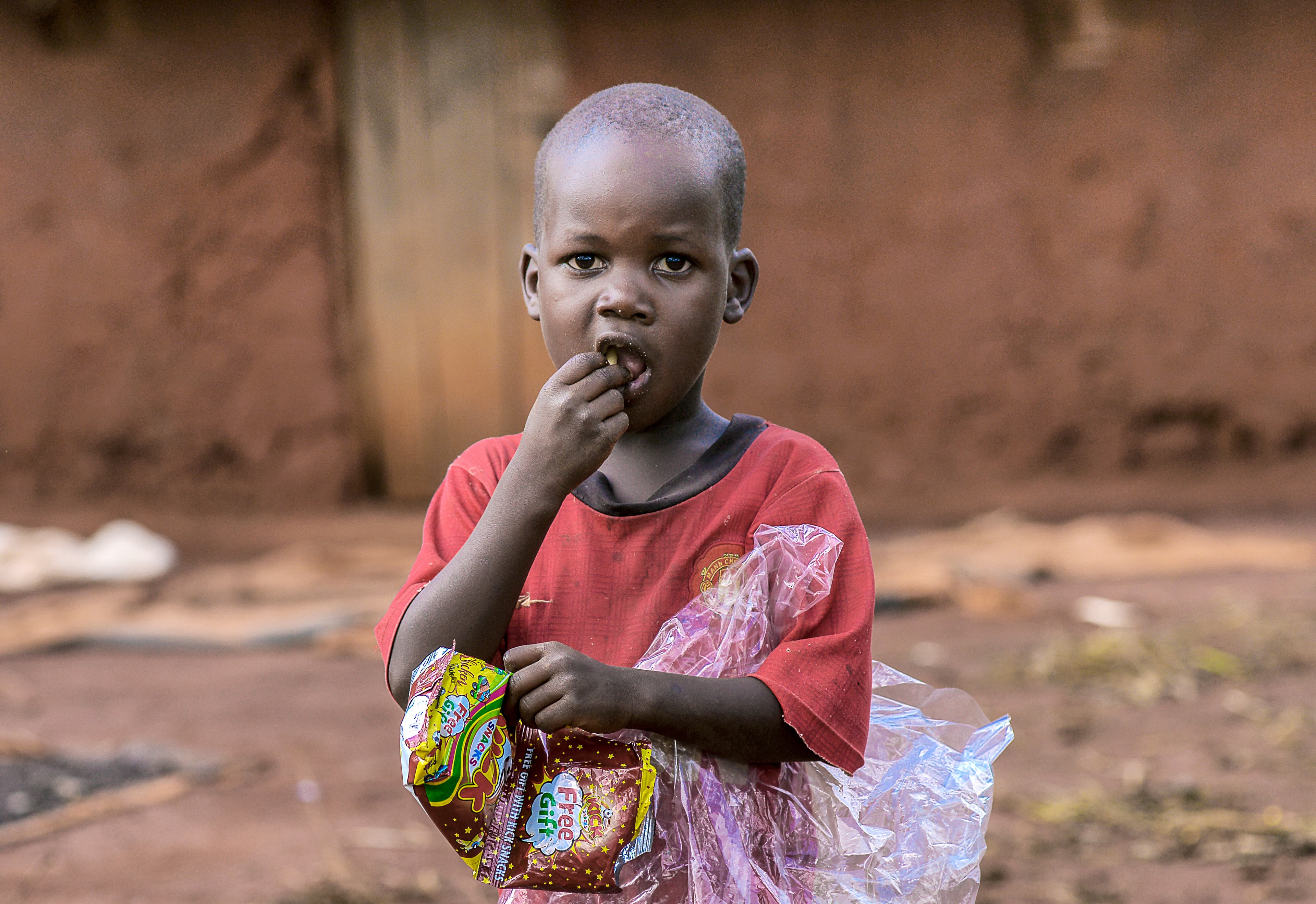 A girl in a red dress stands outdoors holding a small food item.