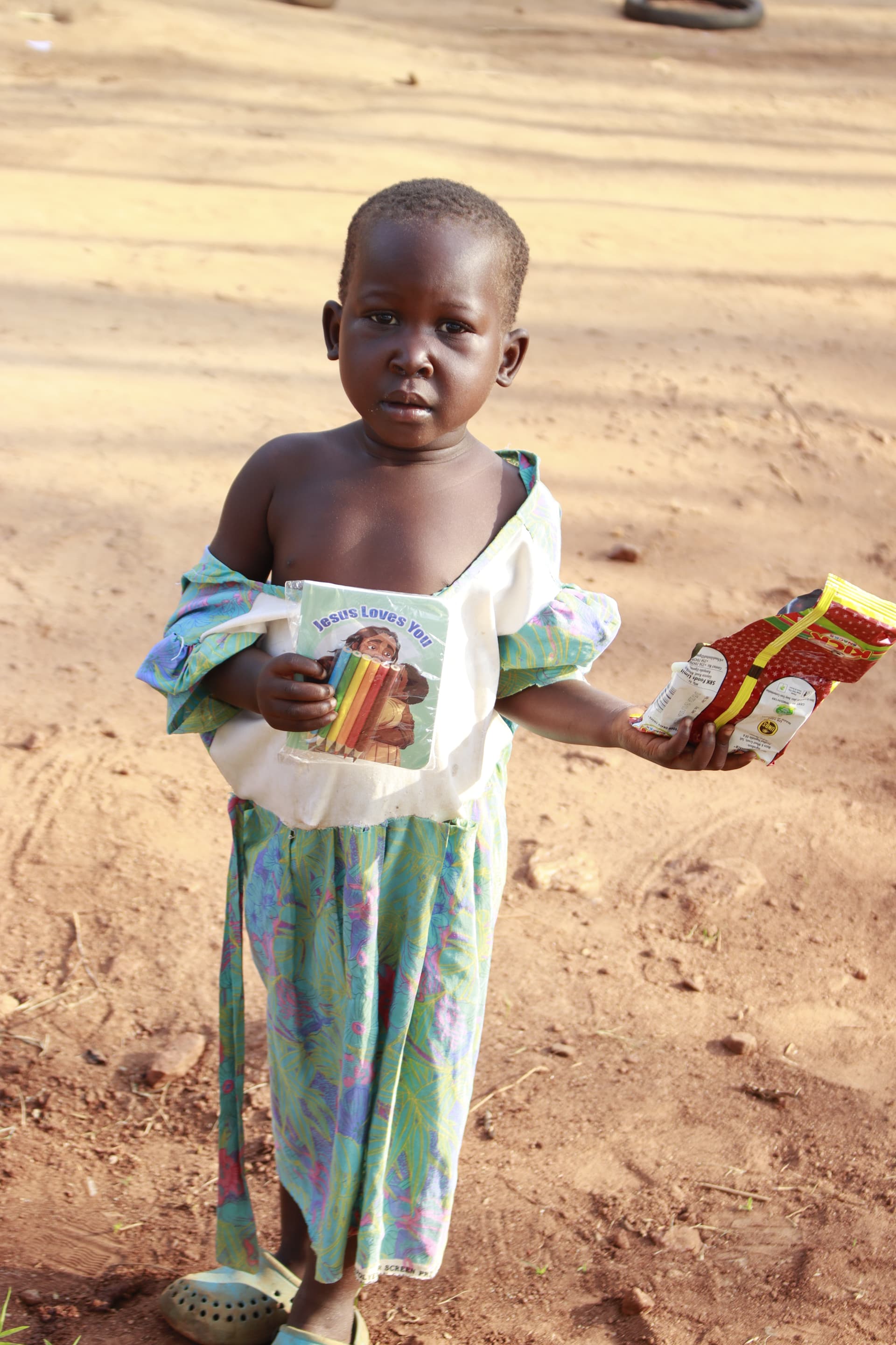 Child carrying a plastic-wrapped bundle of food along a dirt path