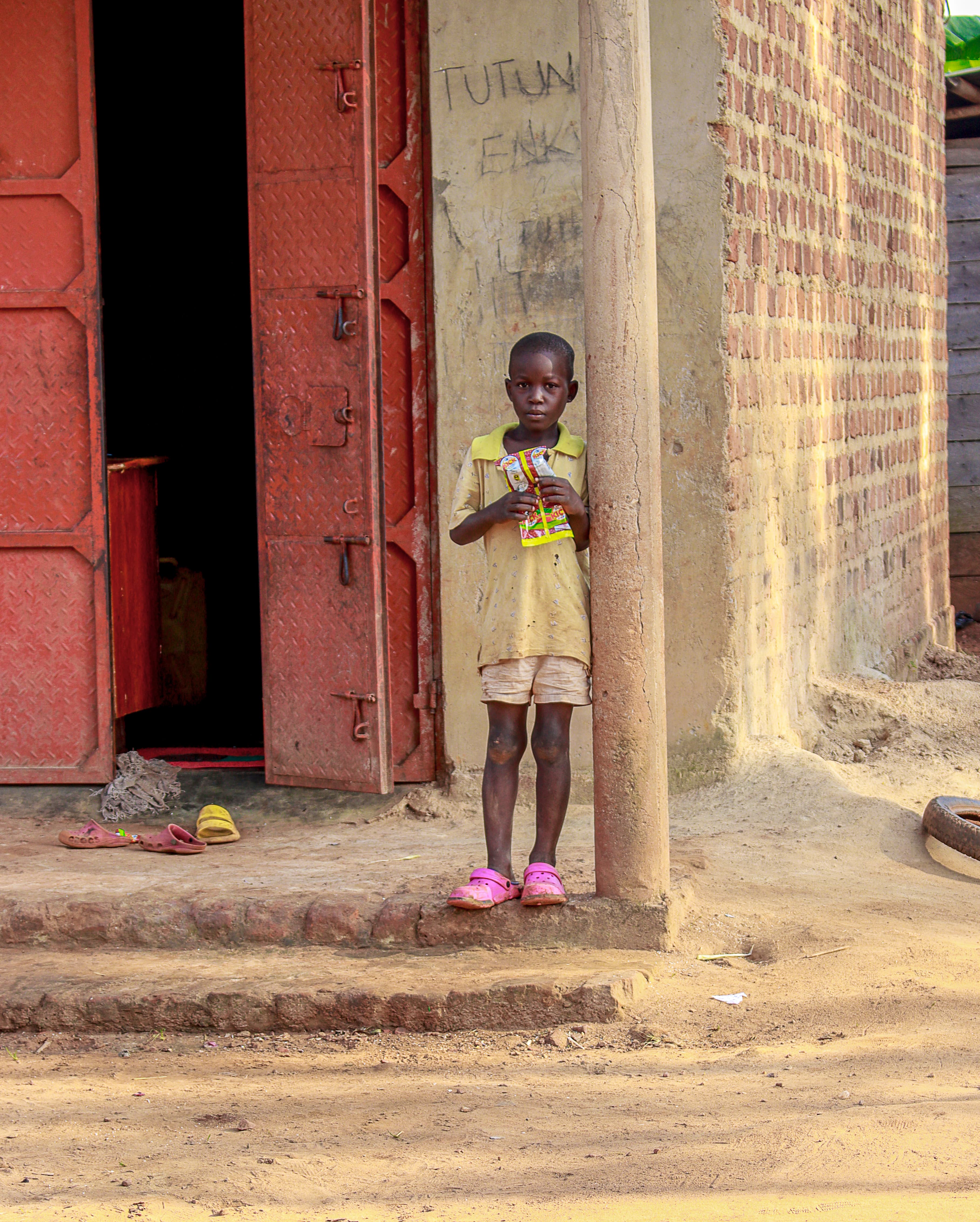 Girl standing in the doorway of a red building holding a small item