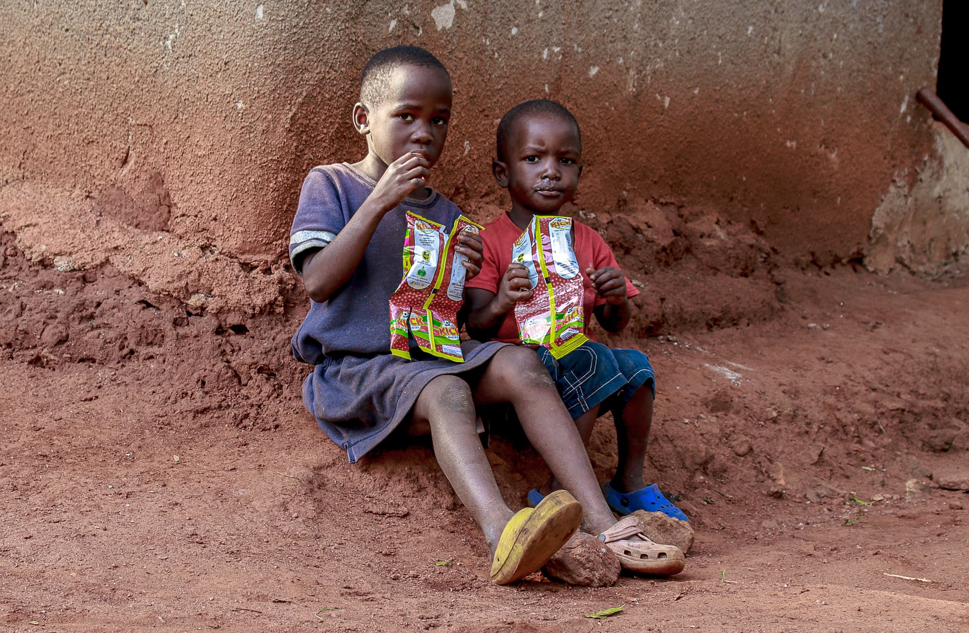 Two children sitting together outdoors eating snacks