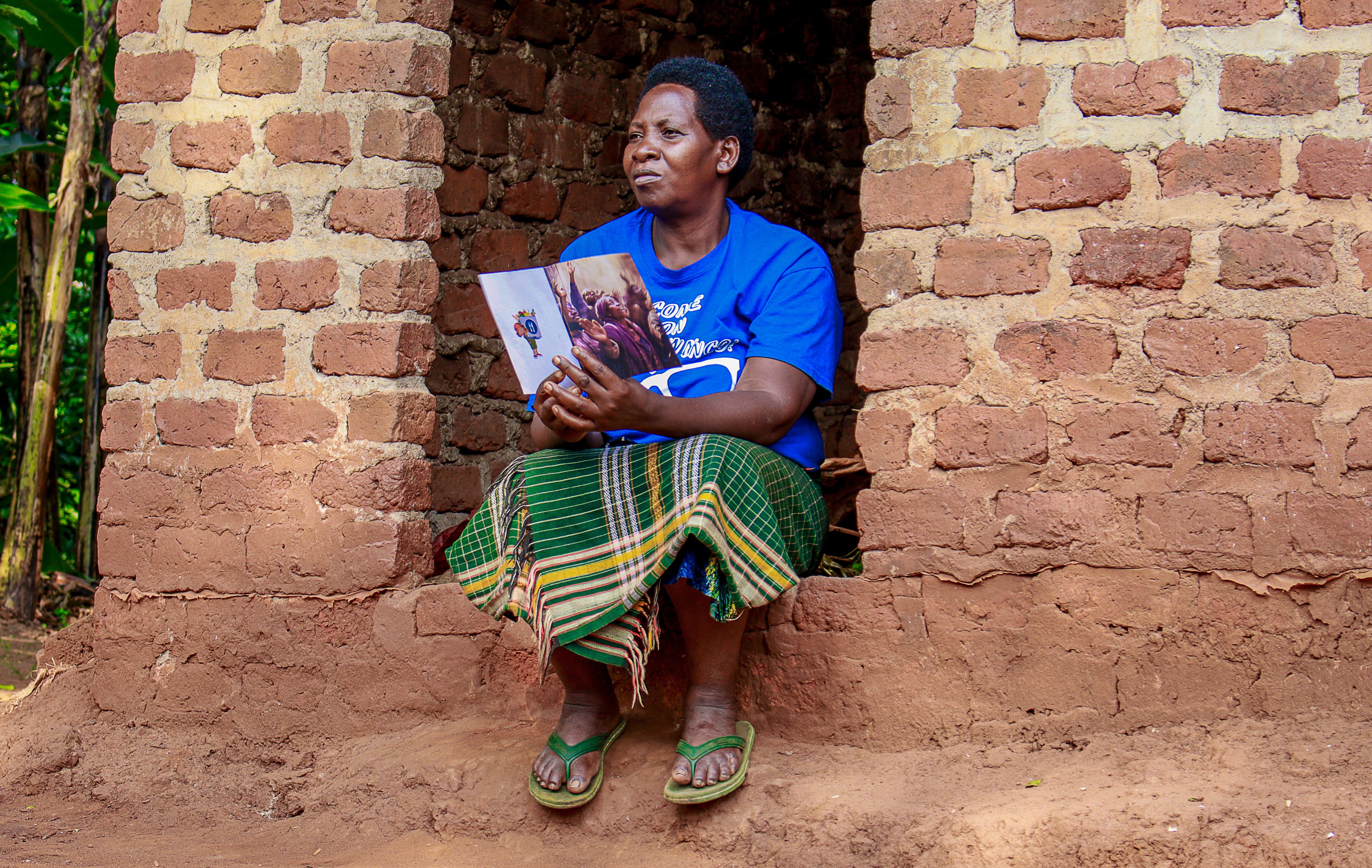 Woman sitting outdoors reading a book near a brick wall