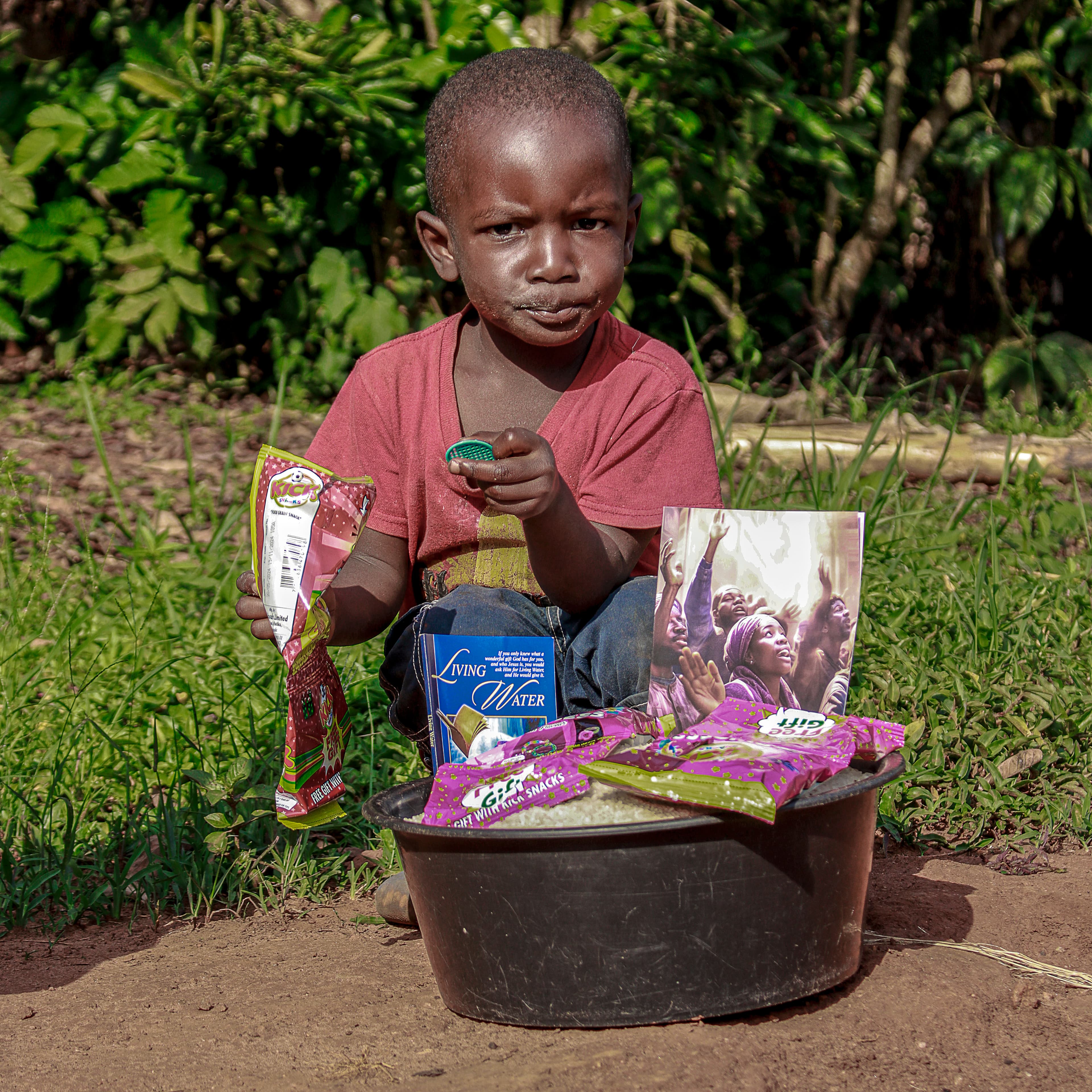 Boy standing outdoors holding a metal basin of food packets and rice