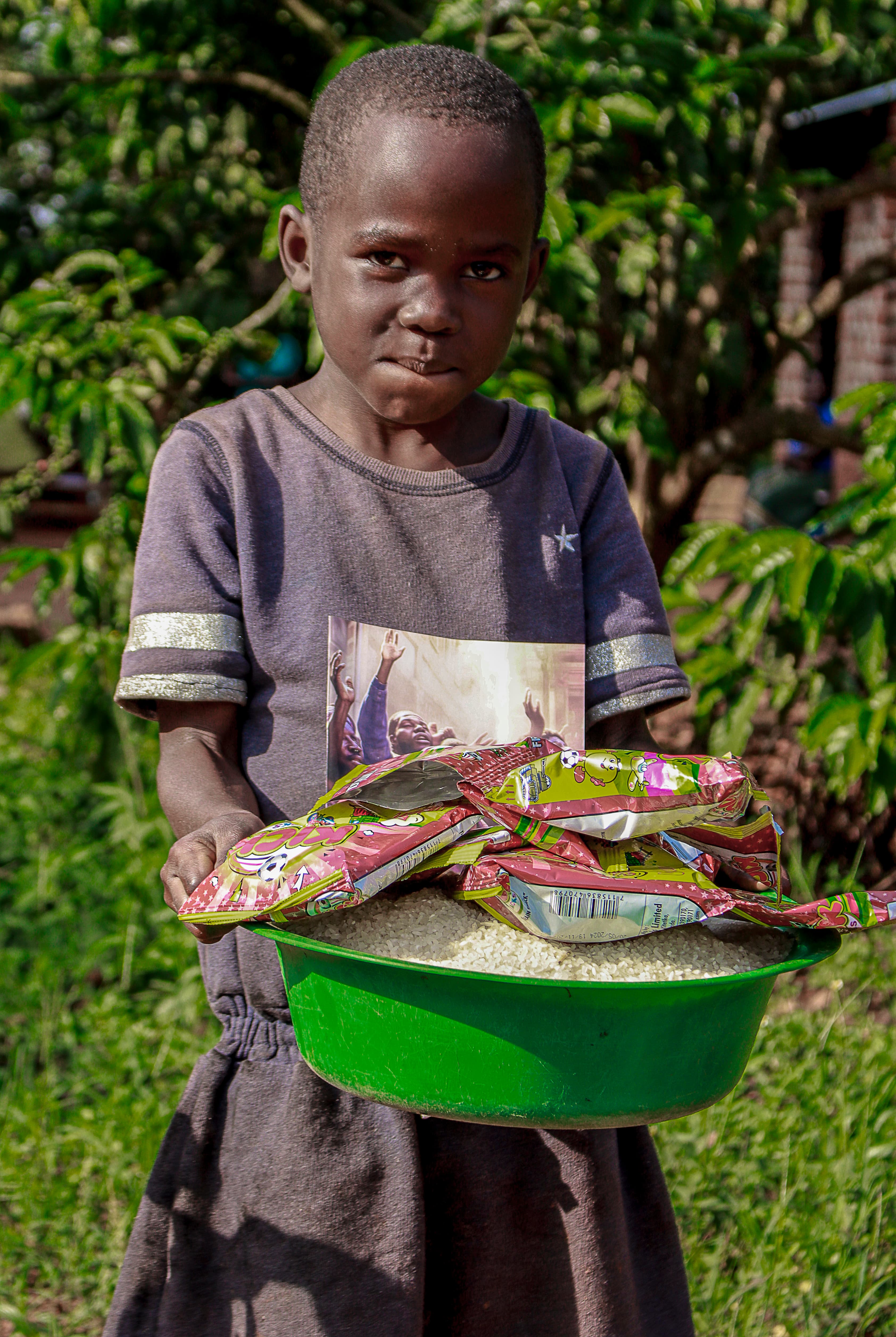 Girl standing outdoors holding a green basin filled with rice