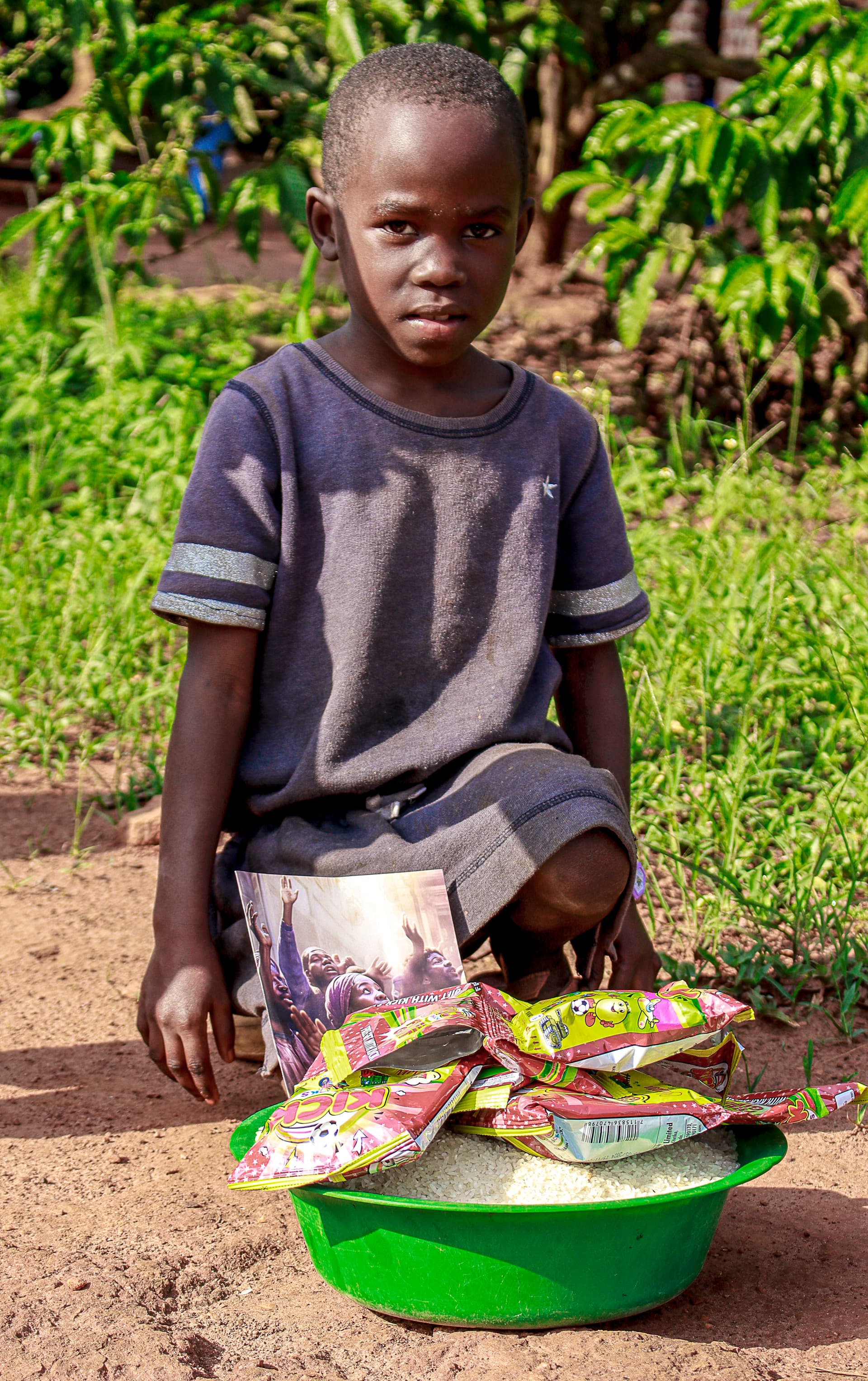 Boy kneeling outdoors with a green basin of rice and food packets