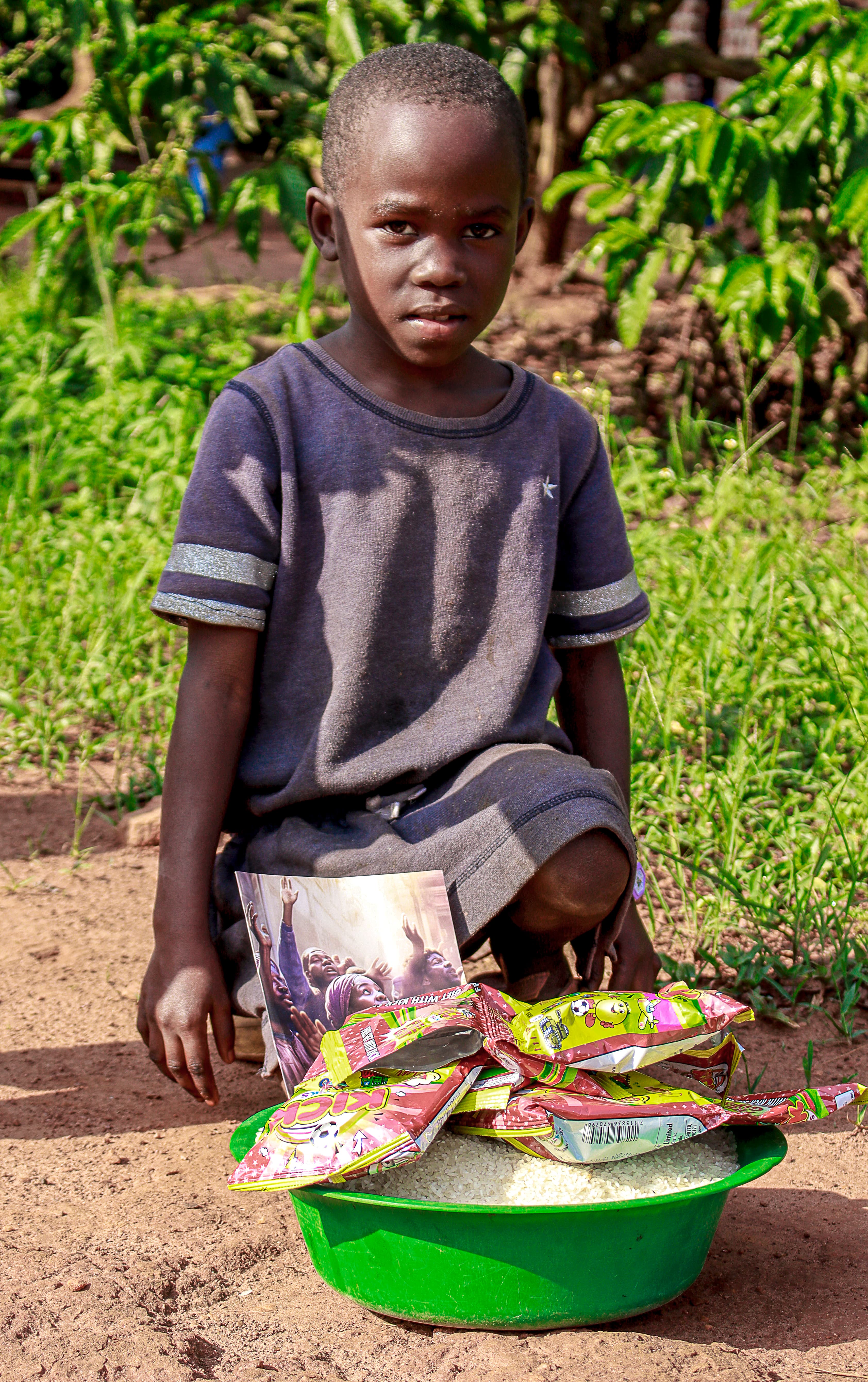 Boy kneeling outdoors with a green basin of rice and food packets