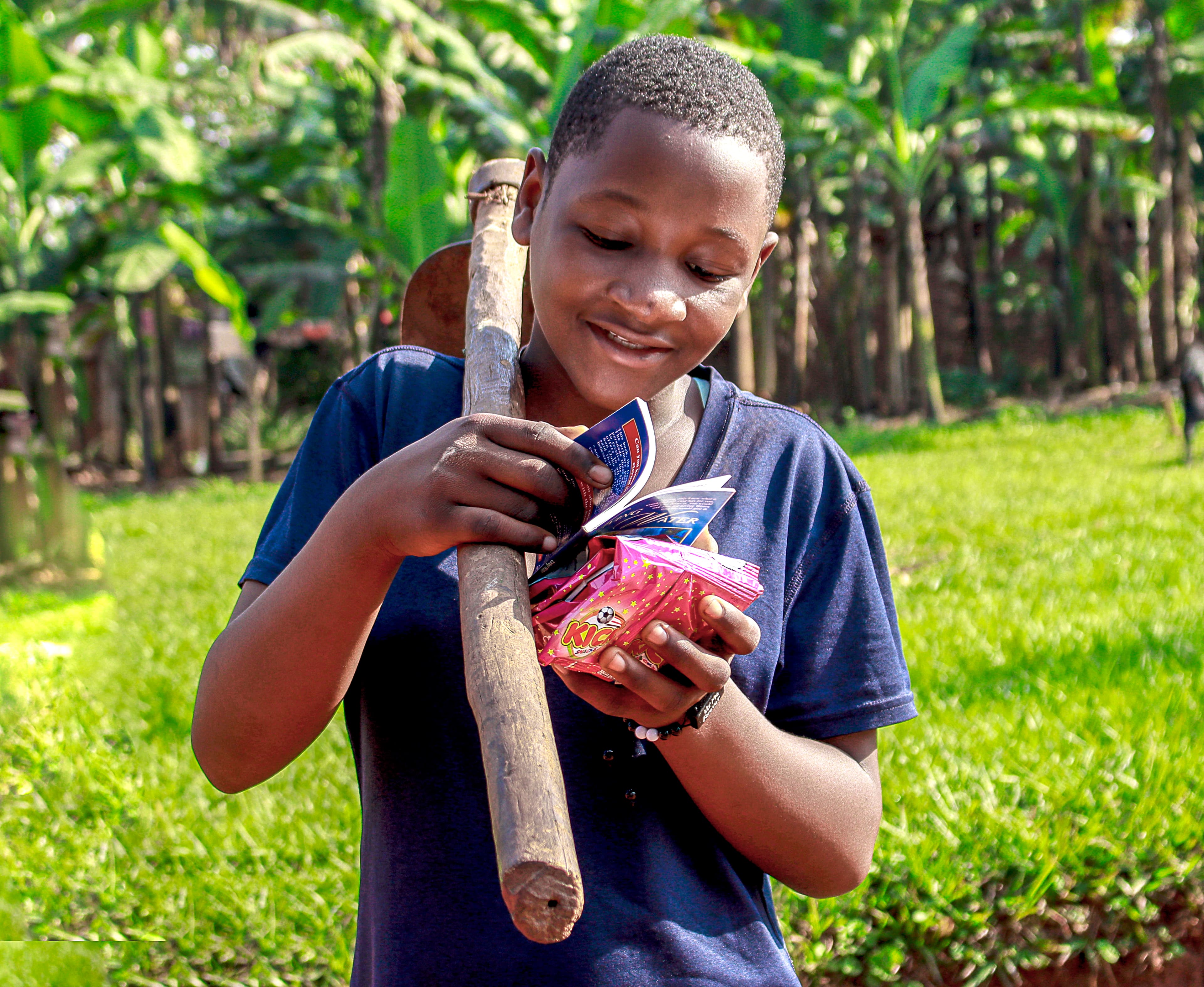 Boy smiling while holding a food packet and a wooden stick outdoors