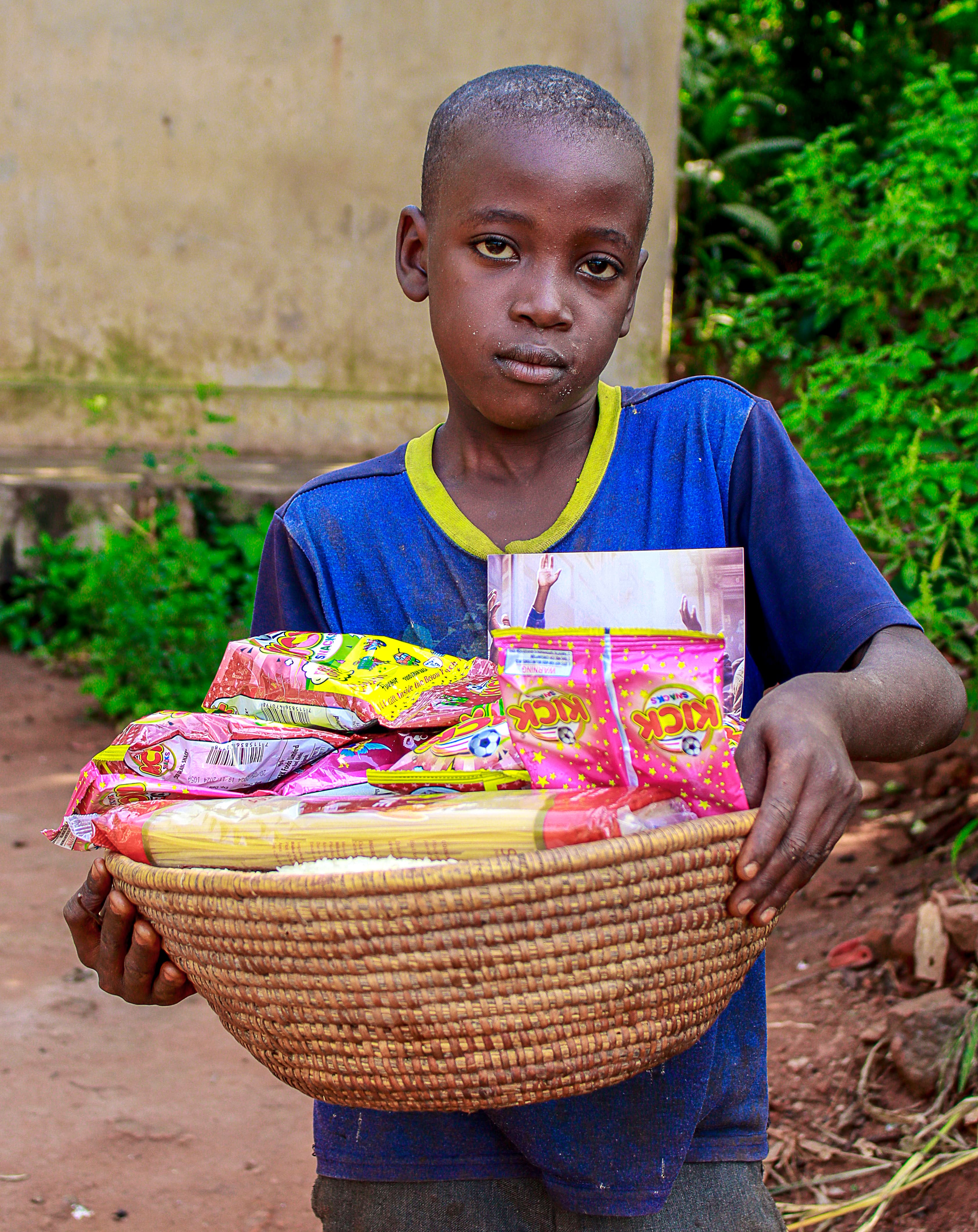 Boy holding a woven basket filled with food packets, standing outdoors