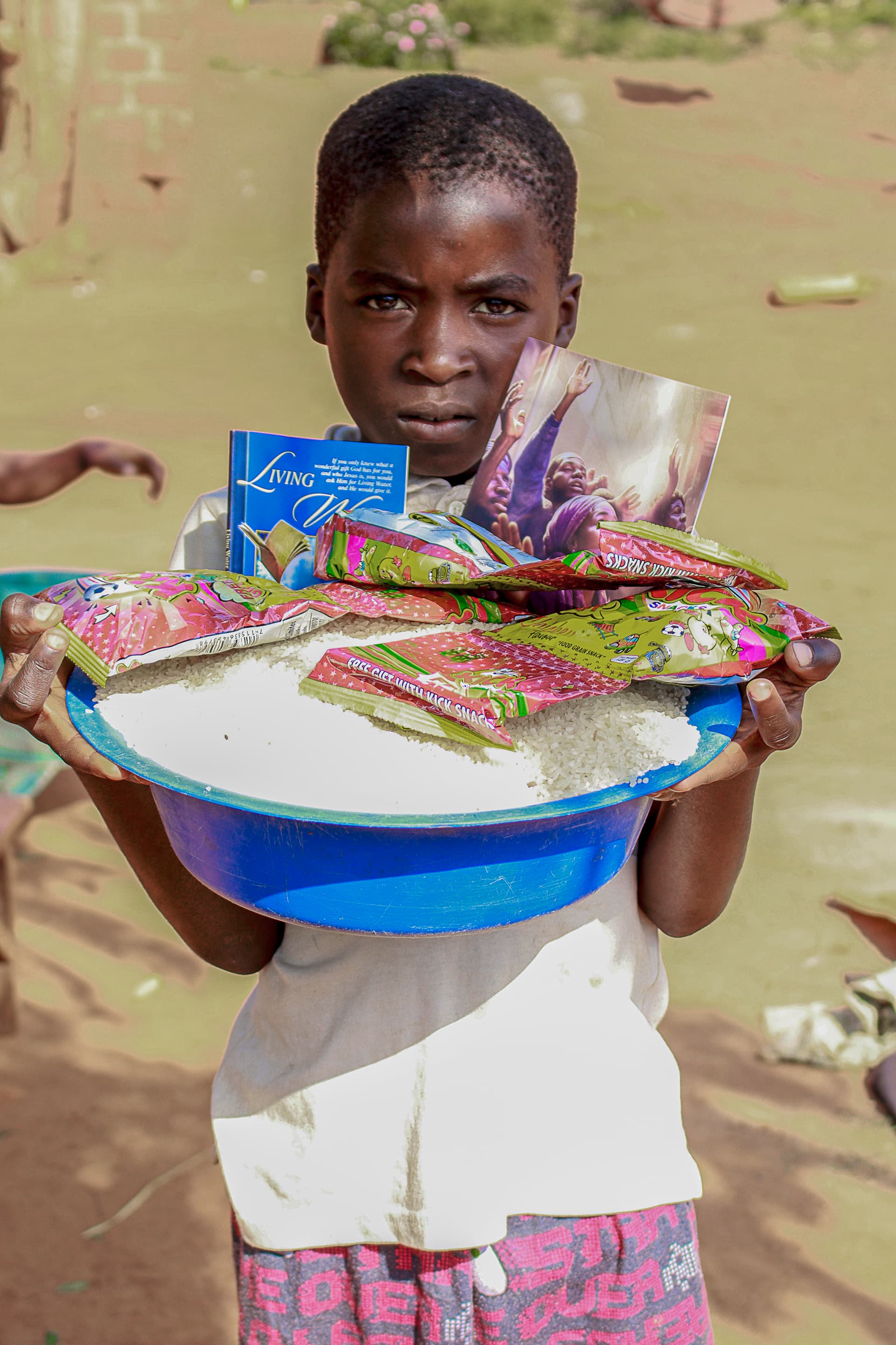 Girl balancing a white basin of food on her head outdoors