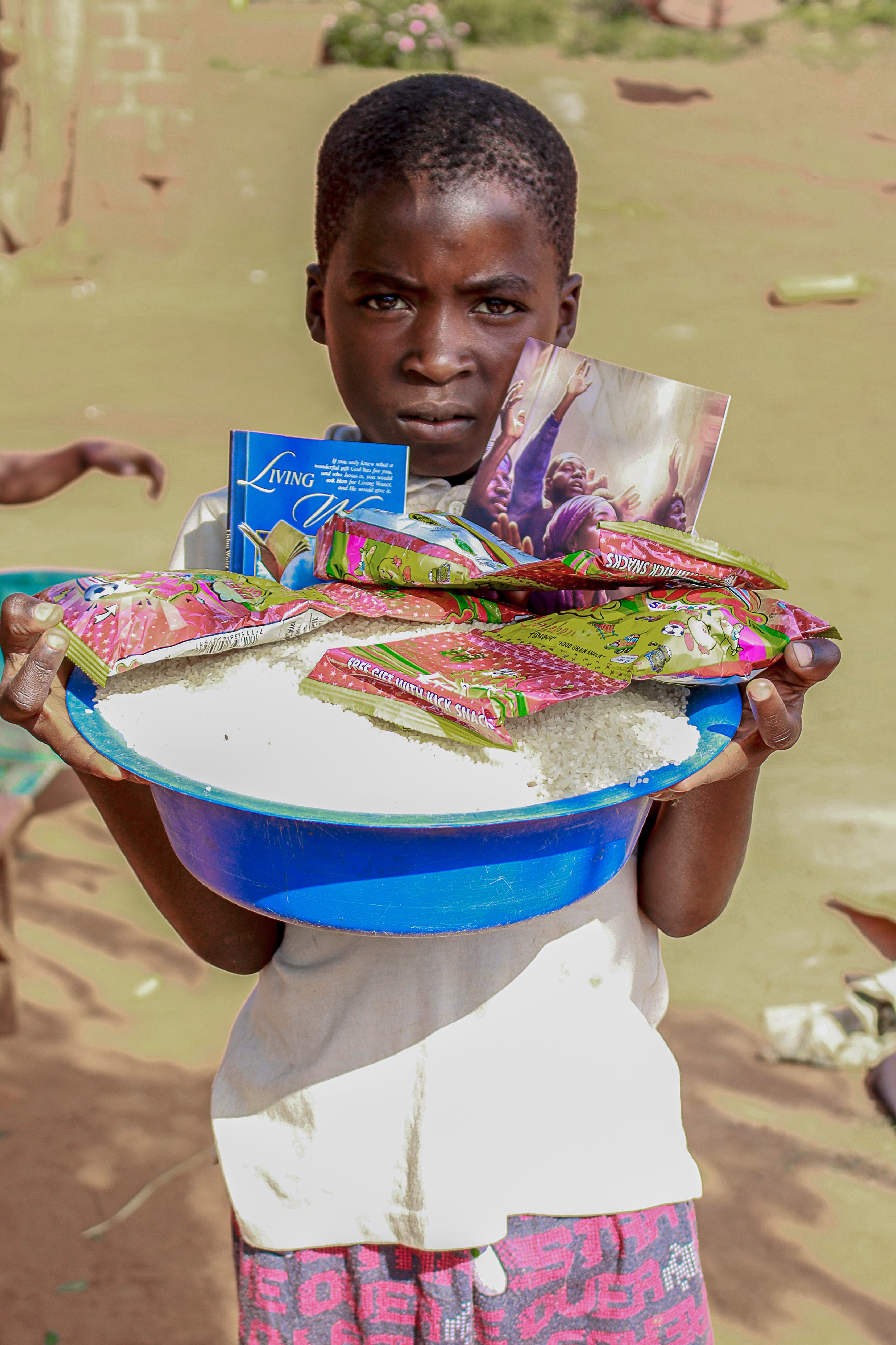 Girl balancing a white basin of food on her head outdoors