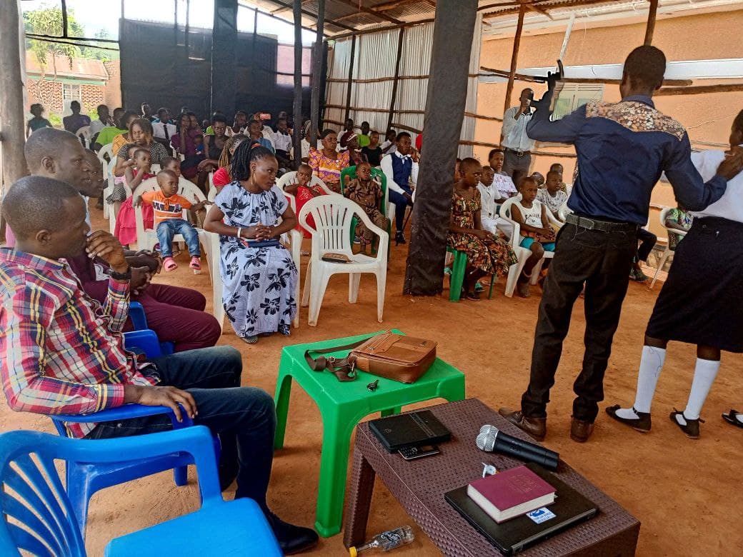Congregation seated in a church hall while a man gestures at the front during a service