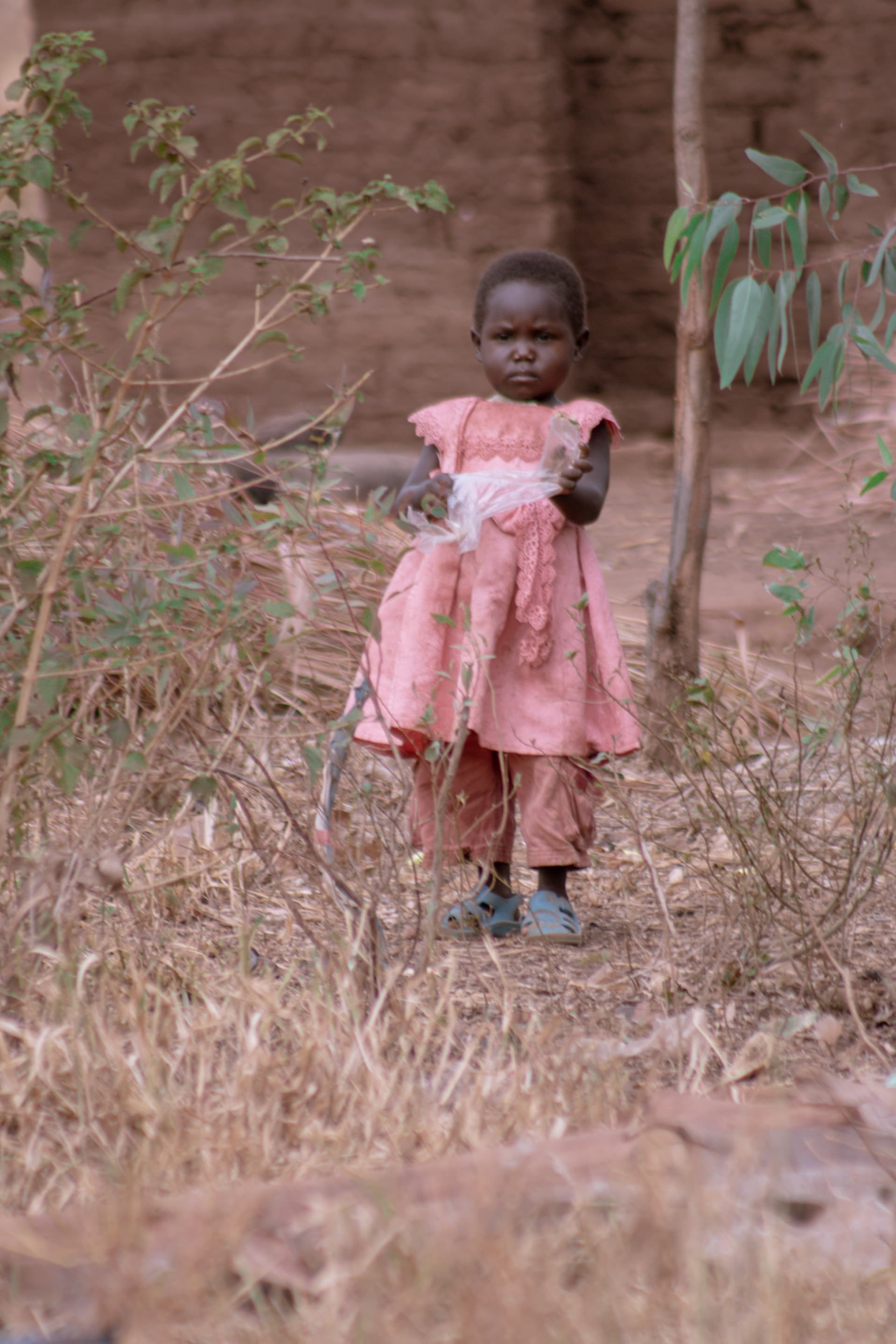 A young girl in a pink dress walking alone along a dirt path.