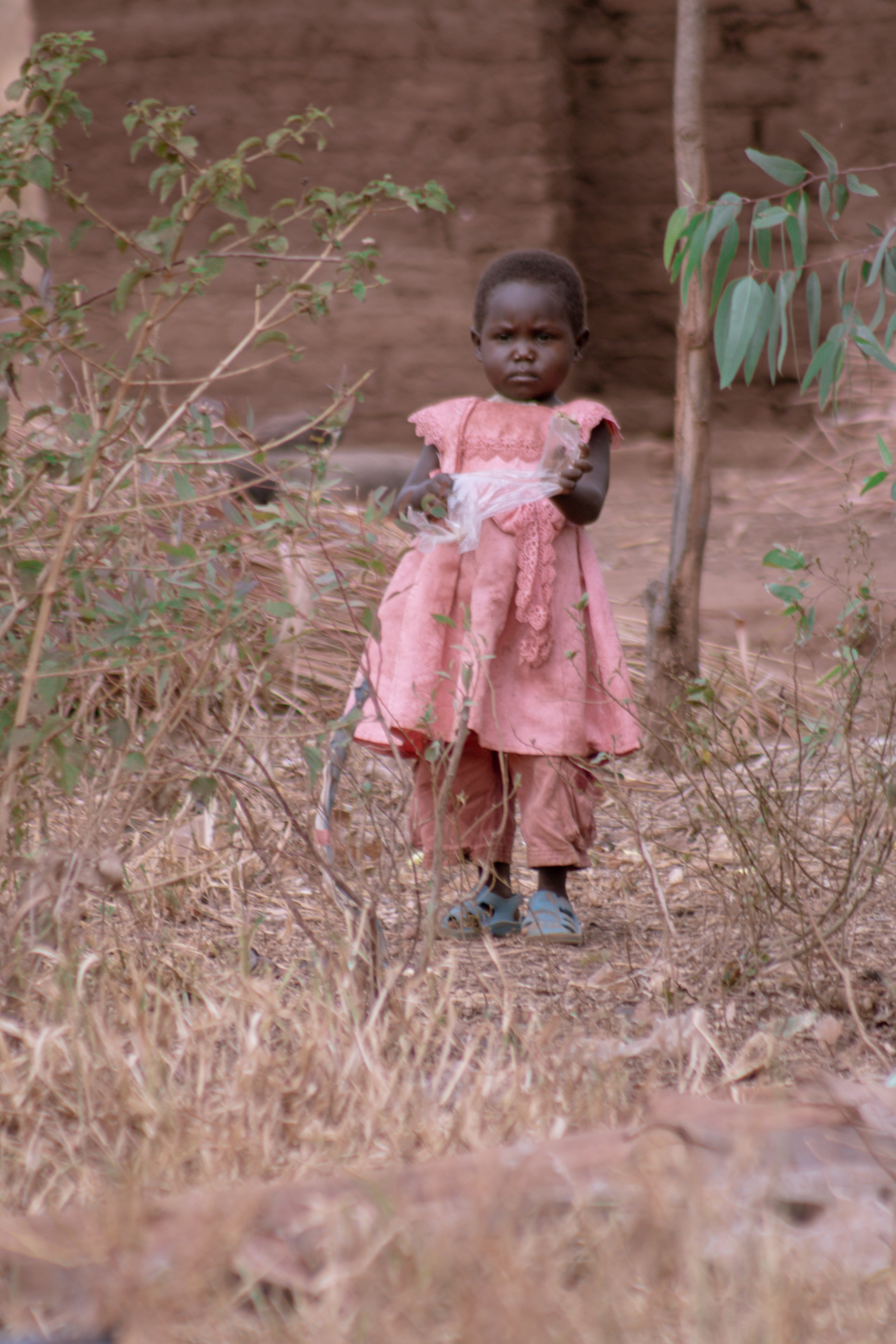 A young girl in a pink dress walking alone along a dirt path.