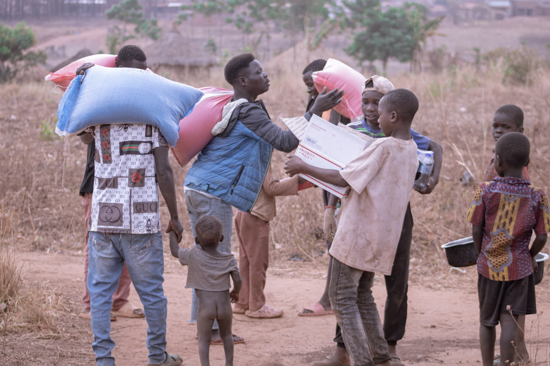 A JFM worker distributes bagged food supplies to children and a woman outdoors.