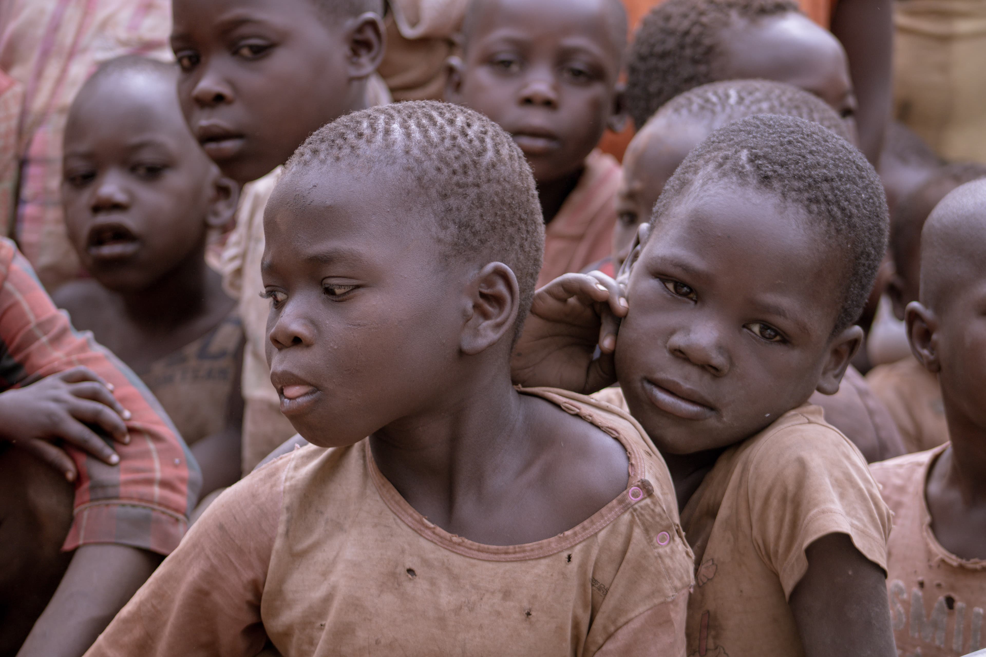 A group of young children stand together outdoors in dry, sparse grassland.