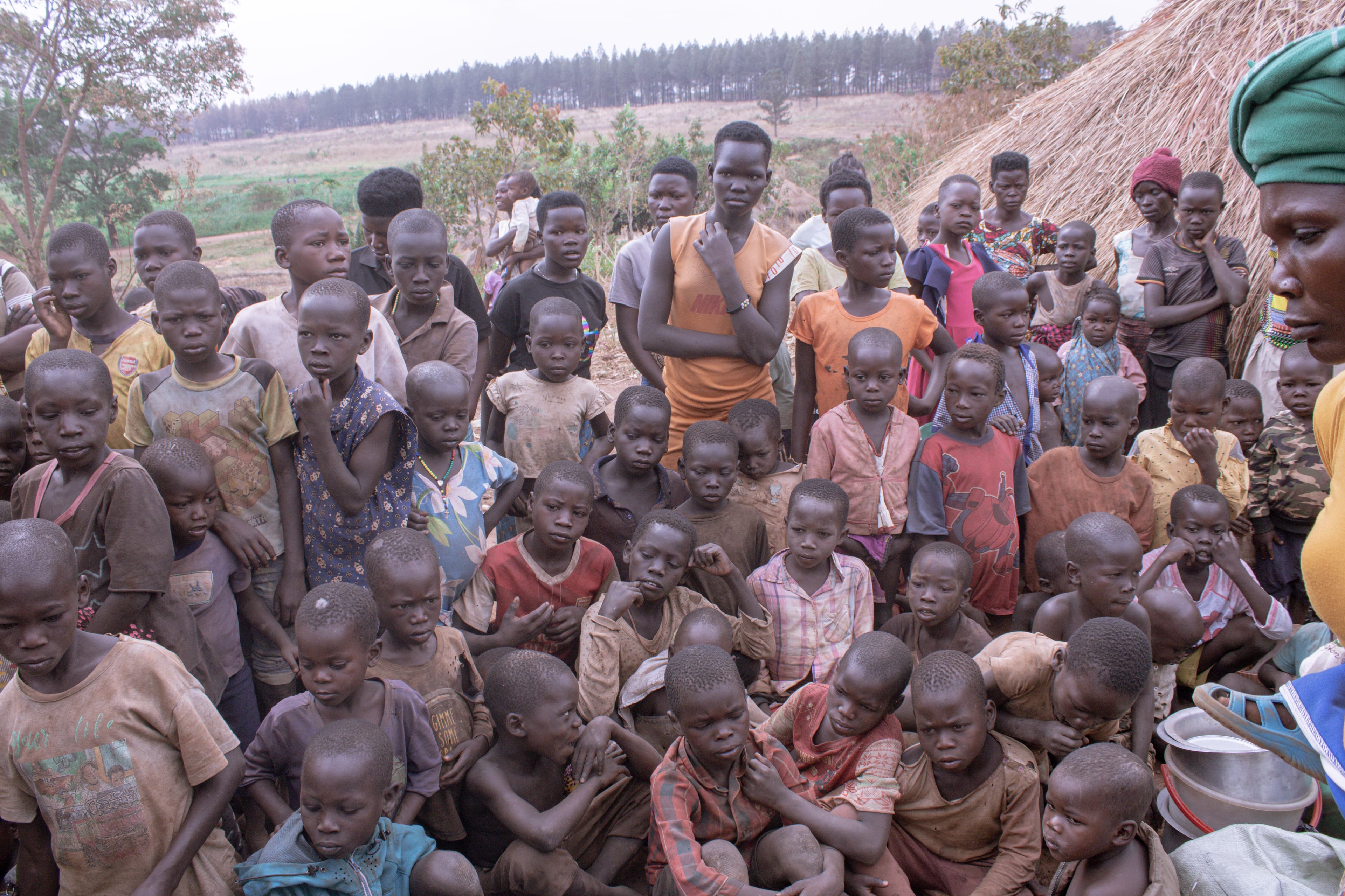 A large group of children and adults gathered together outdoors in the village.