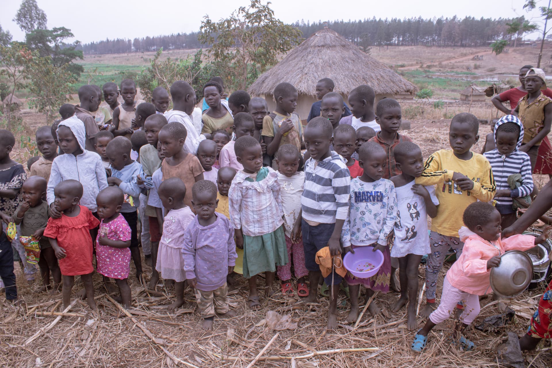 A large group of children gathered outdoors on a hillside near the village.